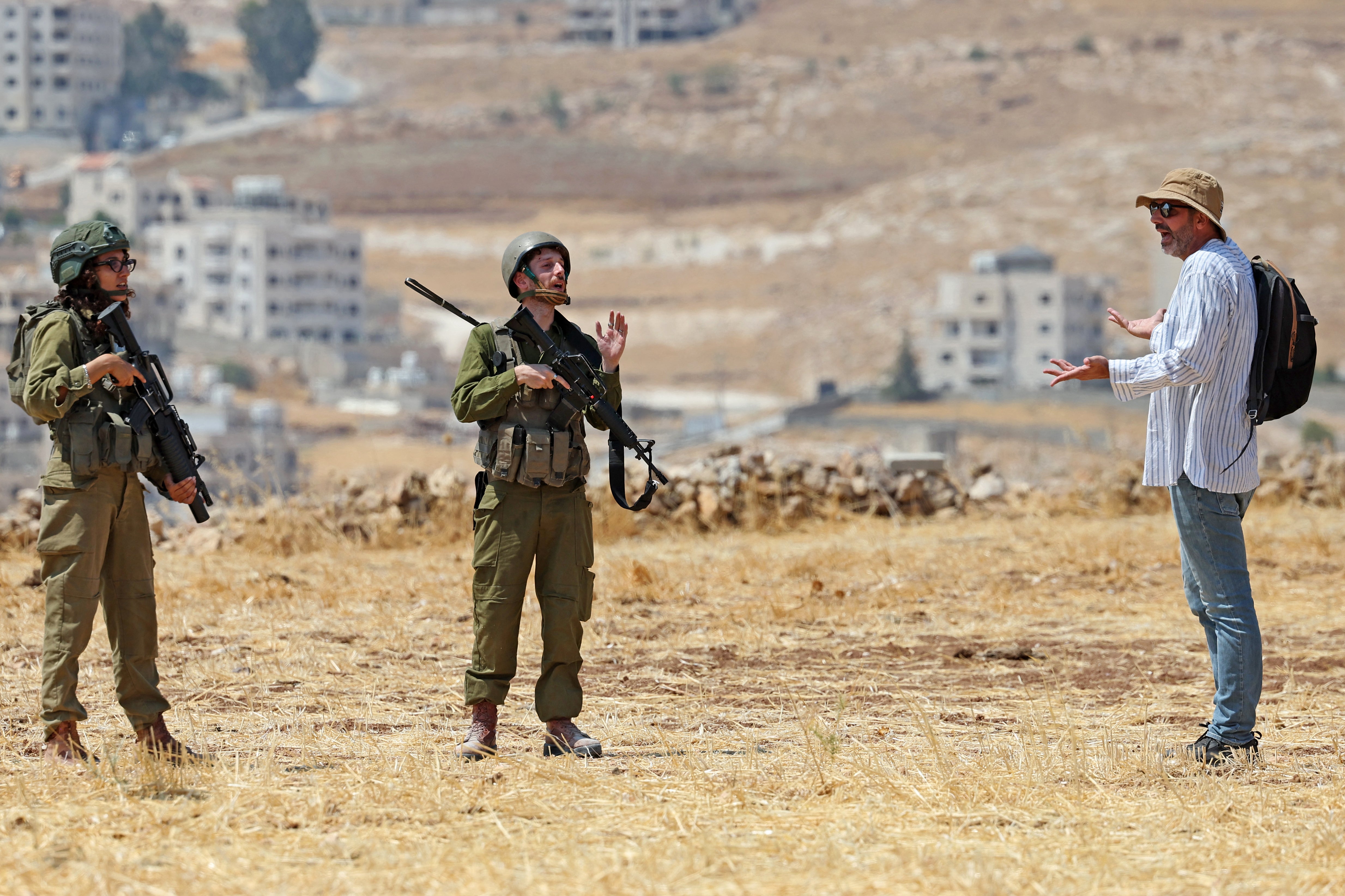 An activist speaks with Israeli soldiers as he accompanies Palestinian landowners to their property, which is at risk of being confiscated by Israeli settlers, in Beit Sahur, south of Bethlehem, in the occupied West Bank on August 14