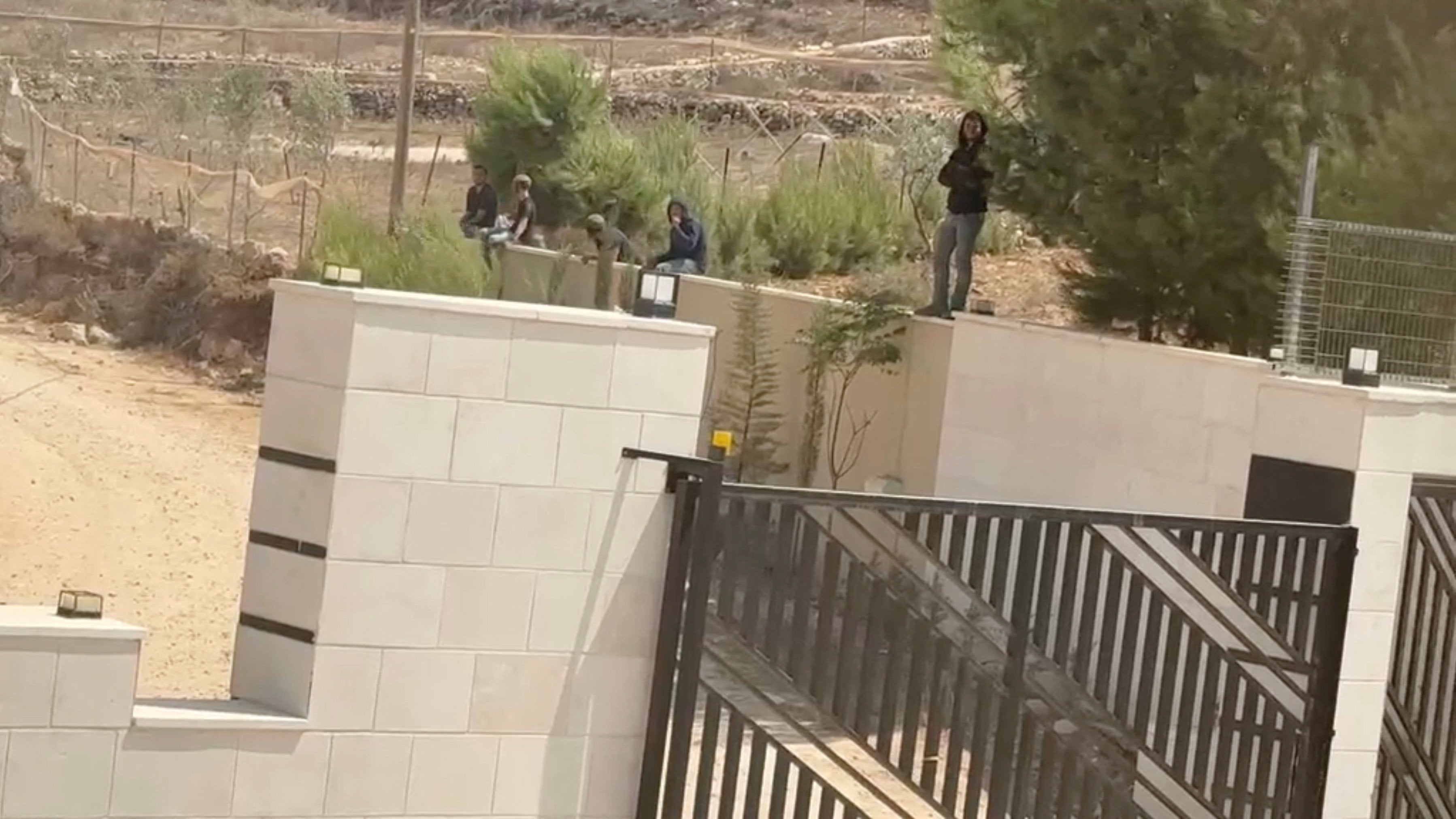 Israeli settlers outside the front gate of a besieged Palestinian home in Qusra