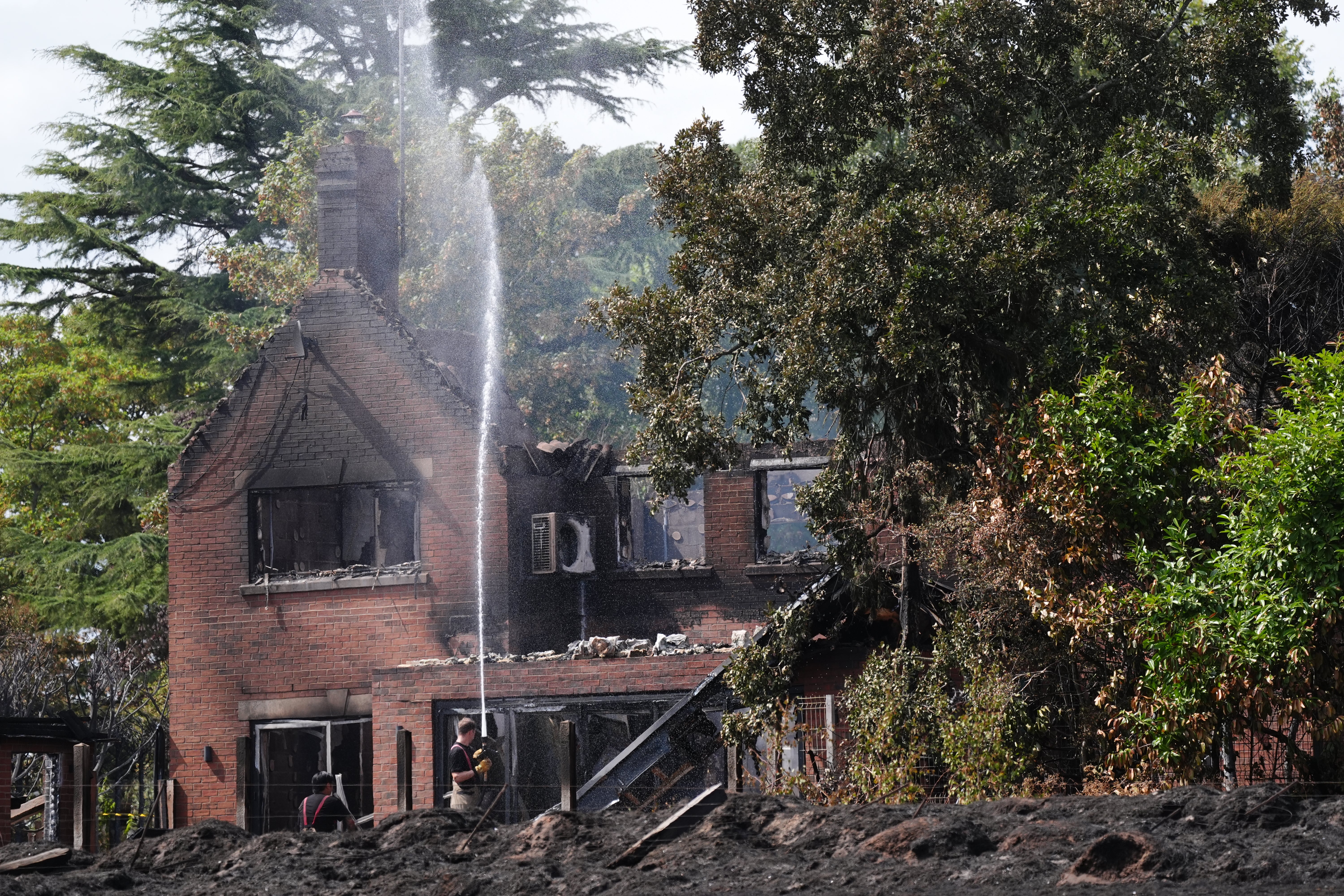 Firefighters spraying water onto the burnt out remains of a house (Jacob King/PA) (PA Wire)