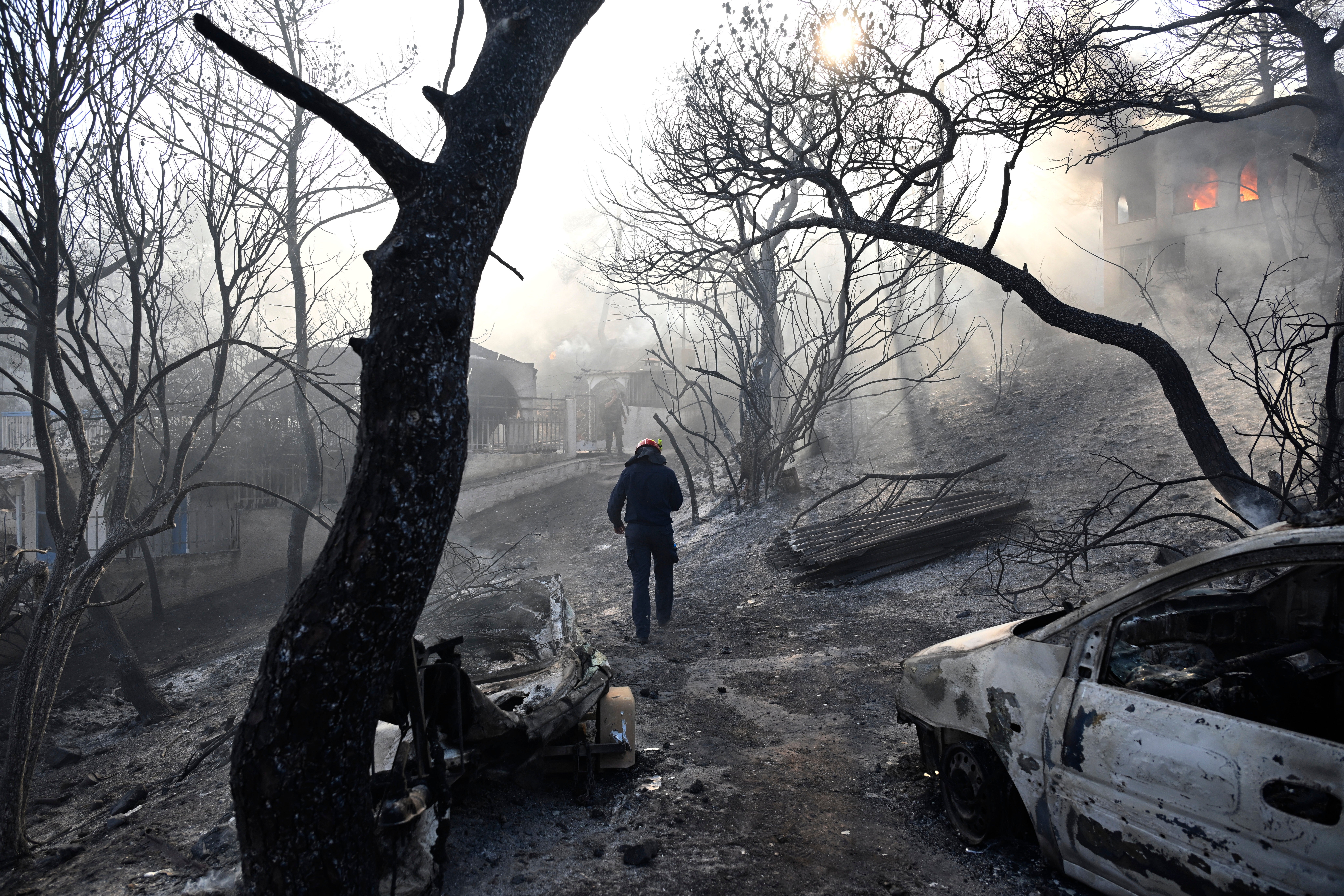 A firefighter walks through a burned area as flames engulf a house during a wildfire on the island of Salamina, west of Athens, Greece