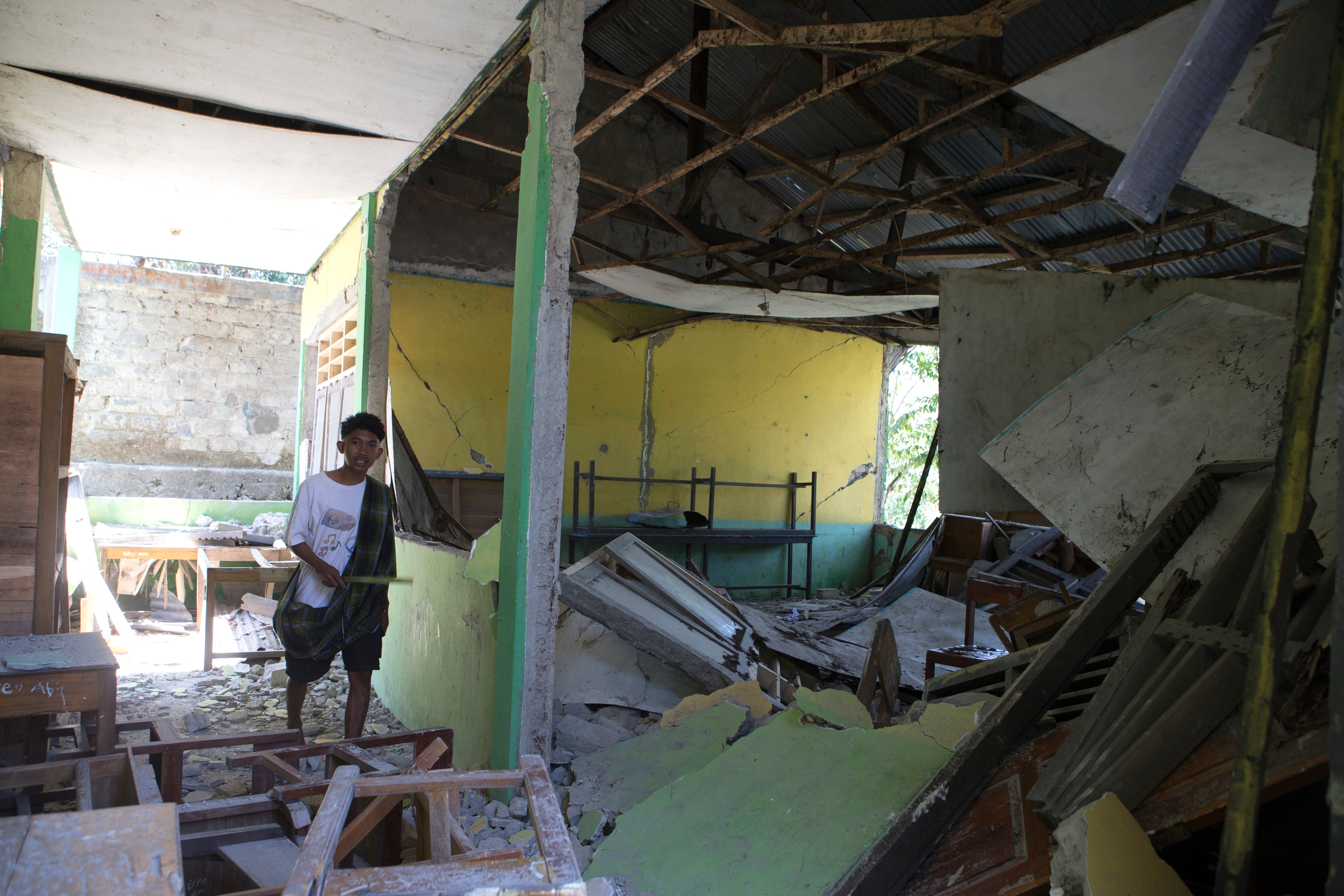 <p>Un joven pasa junto a una escuela dañada durante un terremoto en Reo, provincia de Nusa Tenggara Oriental (Indonesia)</p>