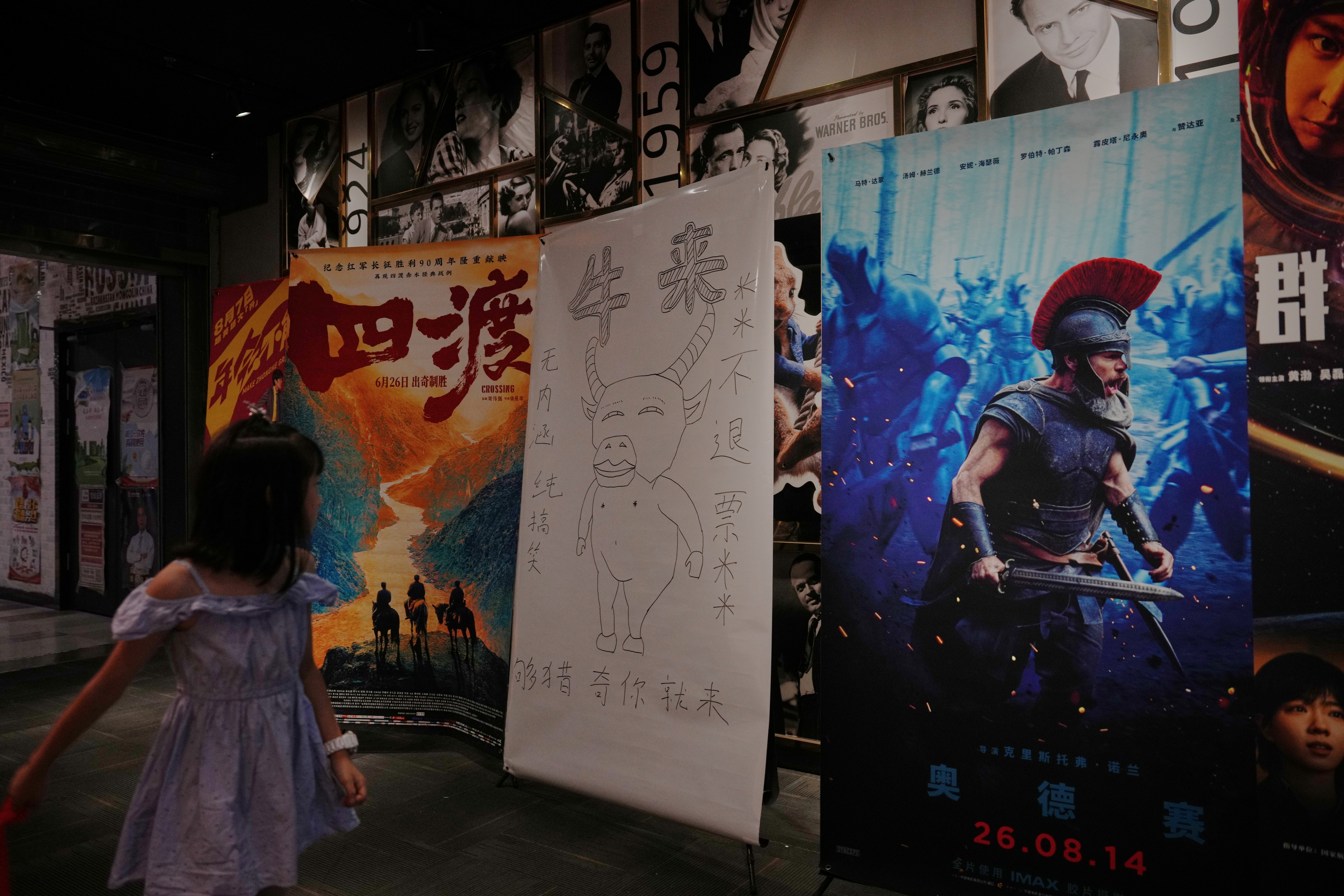 A child looks at a drawing poster promoting a Chinese animated film 'Niulai' on display with other movie posters at a cinema in Beijing, Tuesday, Aug. 18, 2026. (AP Photo/Andy Wong)