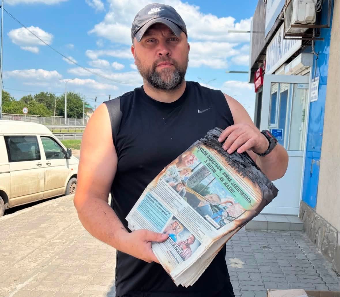 Yevhen Khrypun, chief editor of Mezhivskyi Meridian, holding copies of the newspaper damaged by a Russian attack in Mezhova, Dnipropetrovsk region, August 2026