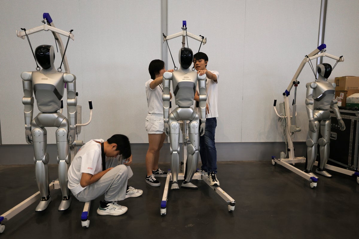 Staff members stand near humanoid robots by LimX Dynamics during the 2026 World Robot Conference, in Beijing (Reuters)