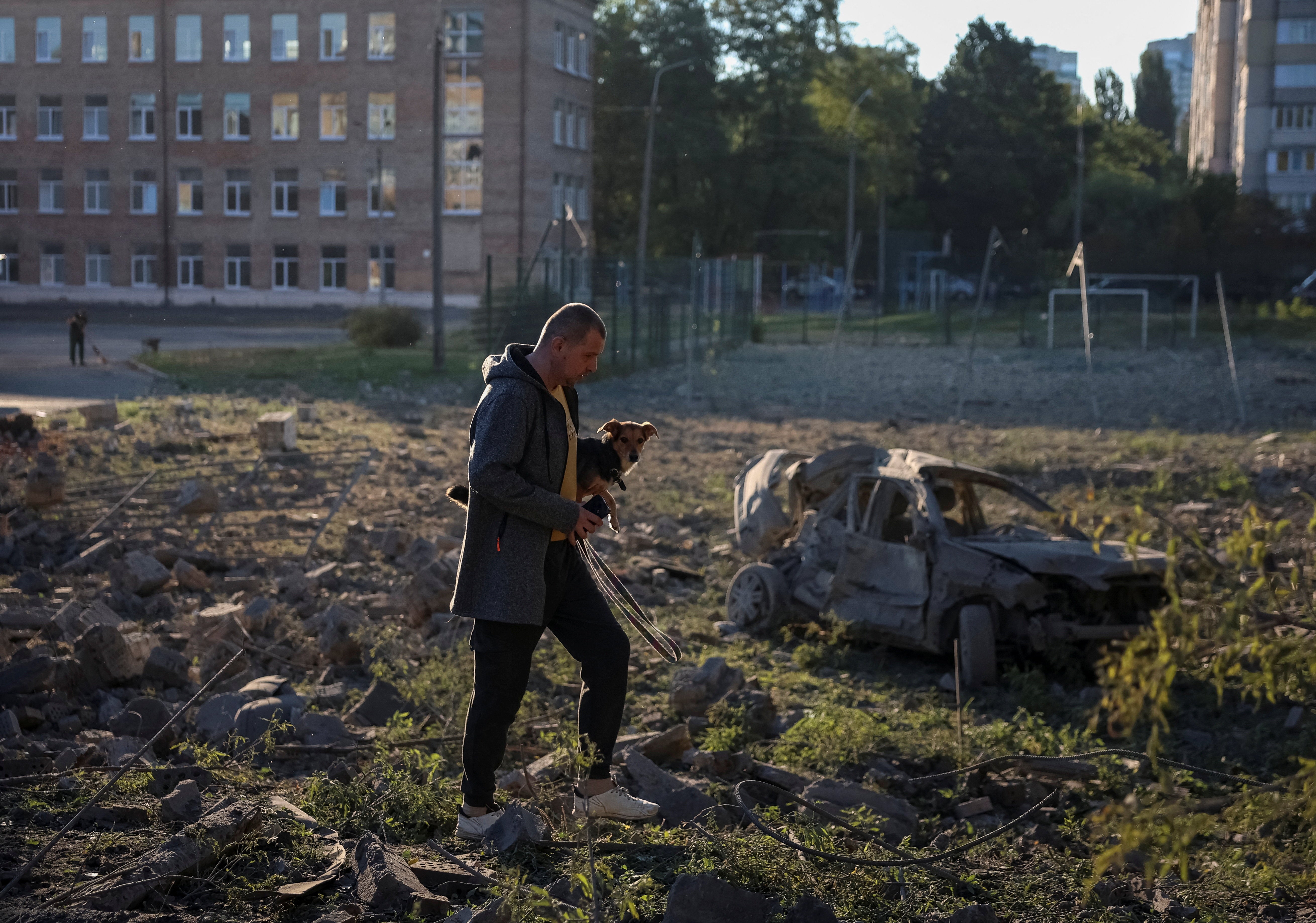 A resident carries a dog as he walks at a site of a Russian missile strike in Kyiv (Reuters)