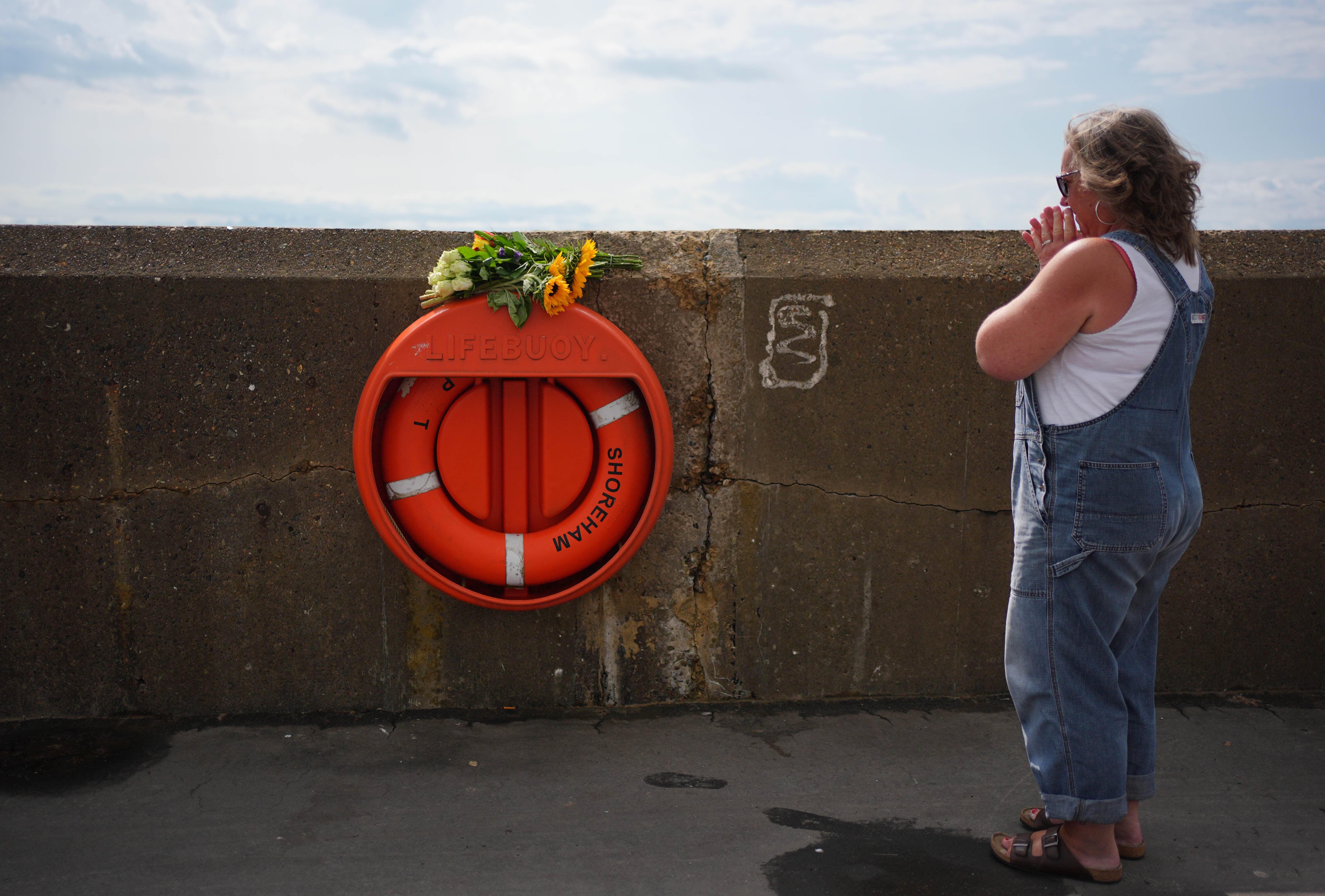 A woman places flowers on a lifebuoy at the beach in Shoreham-by-Sea (Yui Mok/PA) (PA Wire)