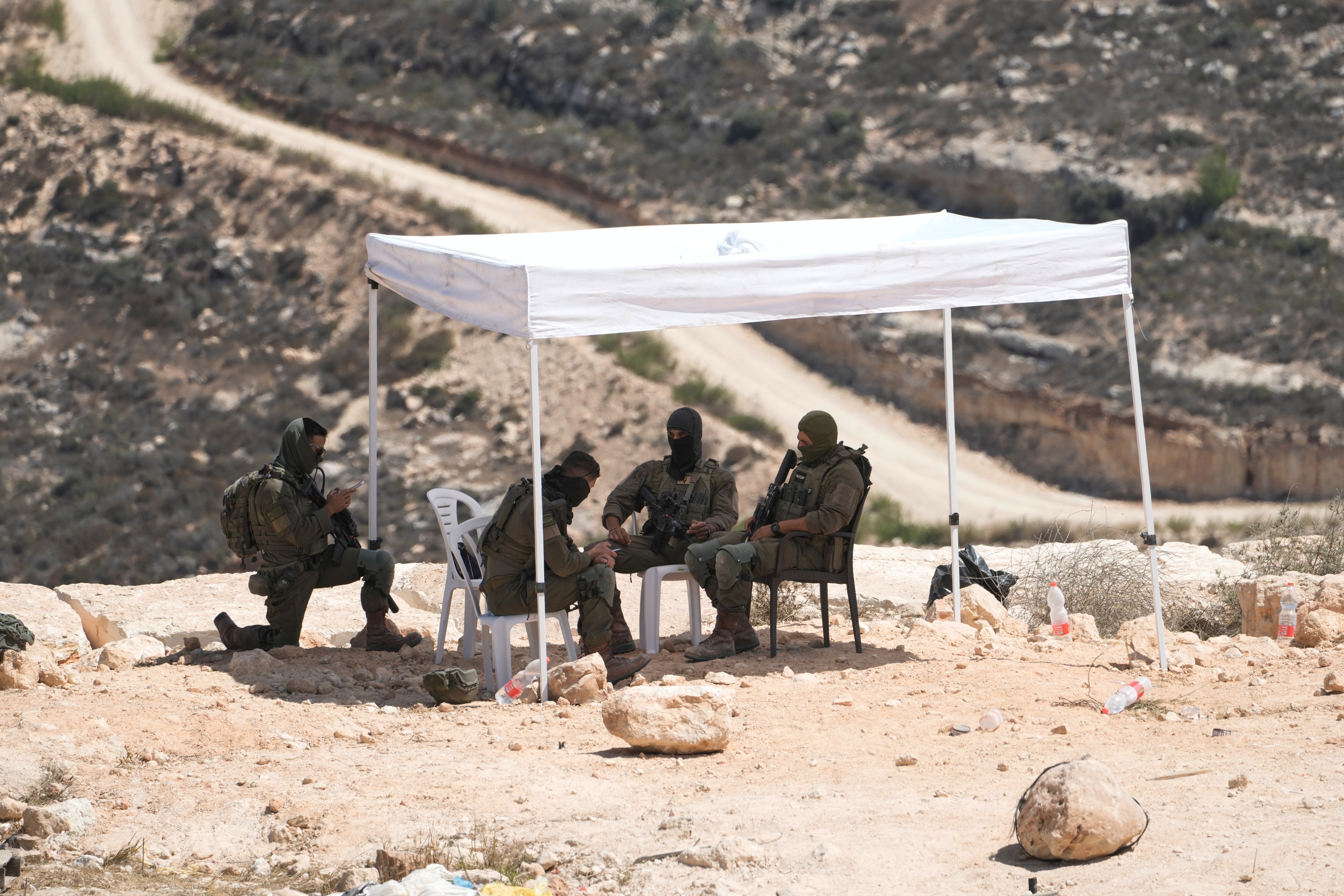 Israeli soldiers sit under a tent in front of the home of Ohio-based Palestinian American landlord Loui Ridi, which has been besieged by Israeli settlers for over a week