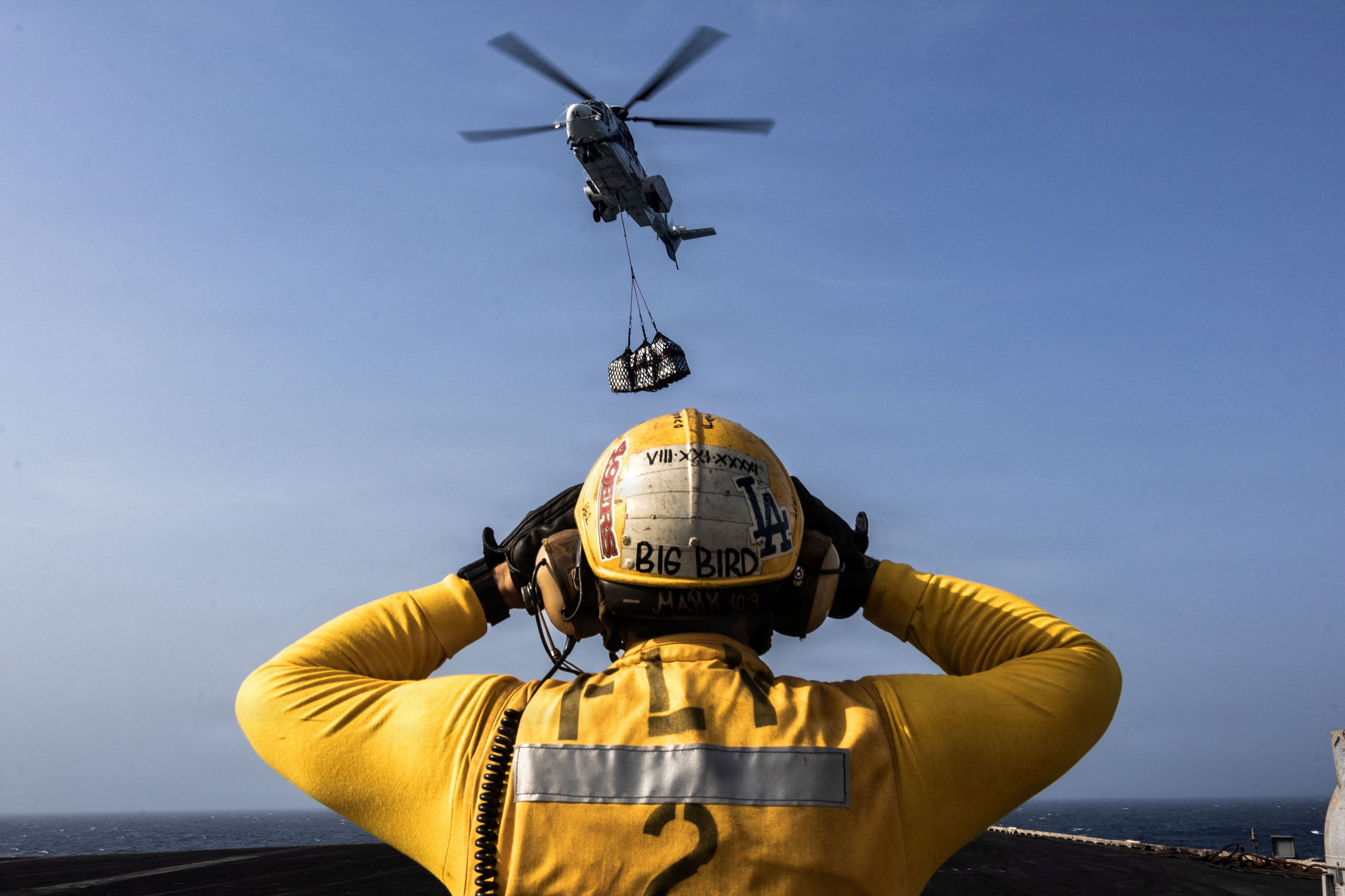 A sailor directs a military helicopter carrying supplies to the deck of the Lincoln on August 16
