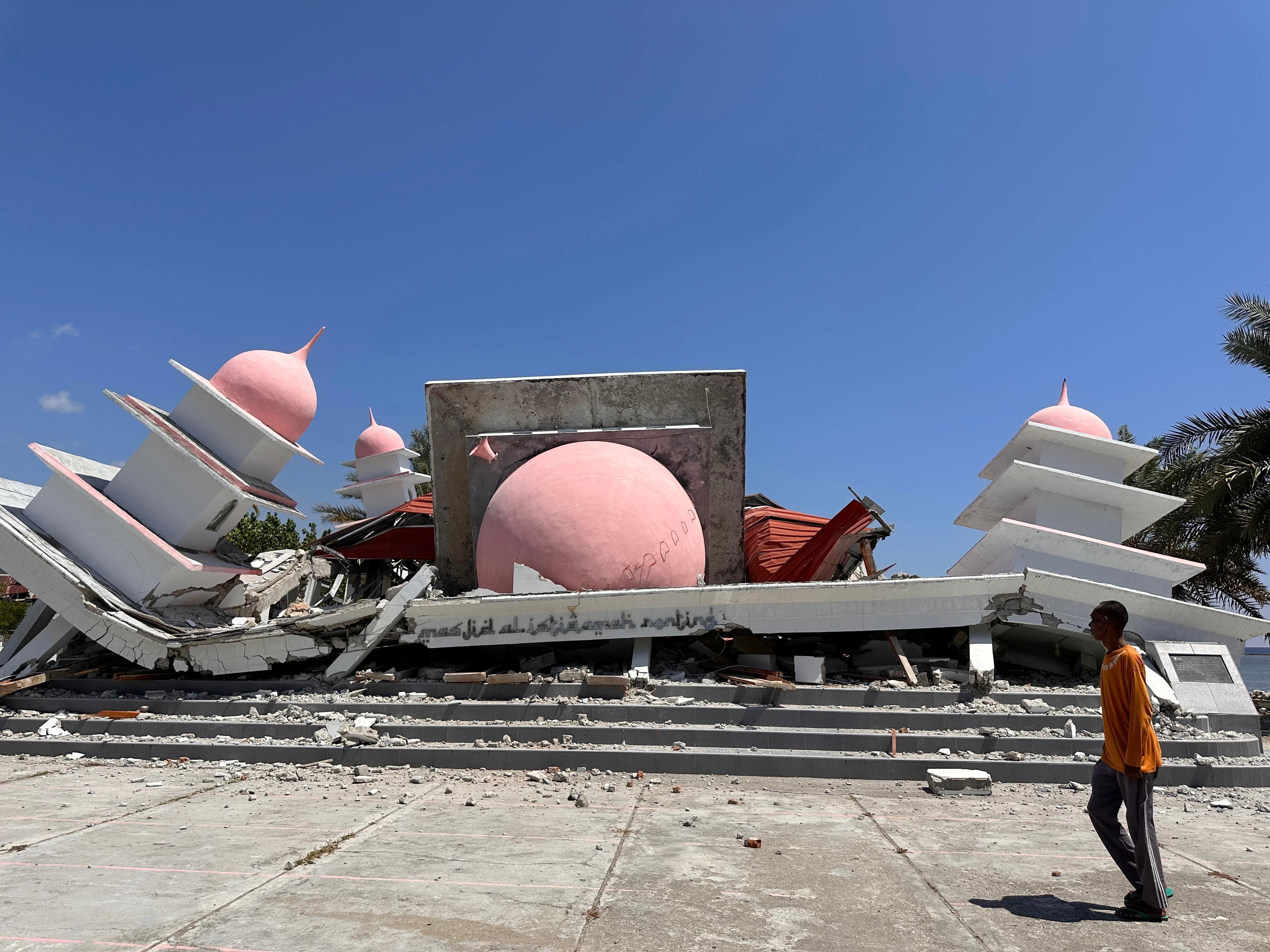 A man walks past a mosque collapsed during an earthquake in Lamba Leda, Indonesia, on Tuesday. Tens of thousands of people were displaced by the quake
