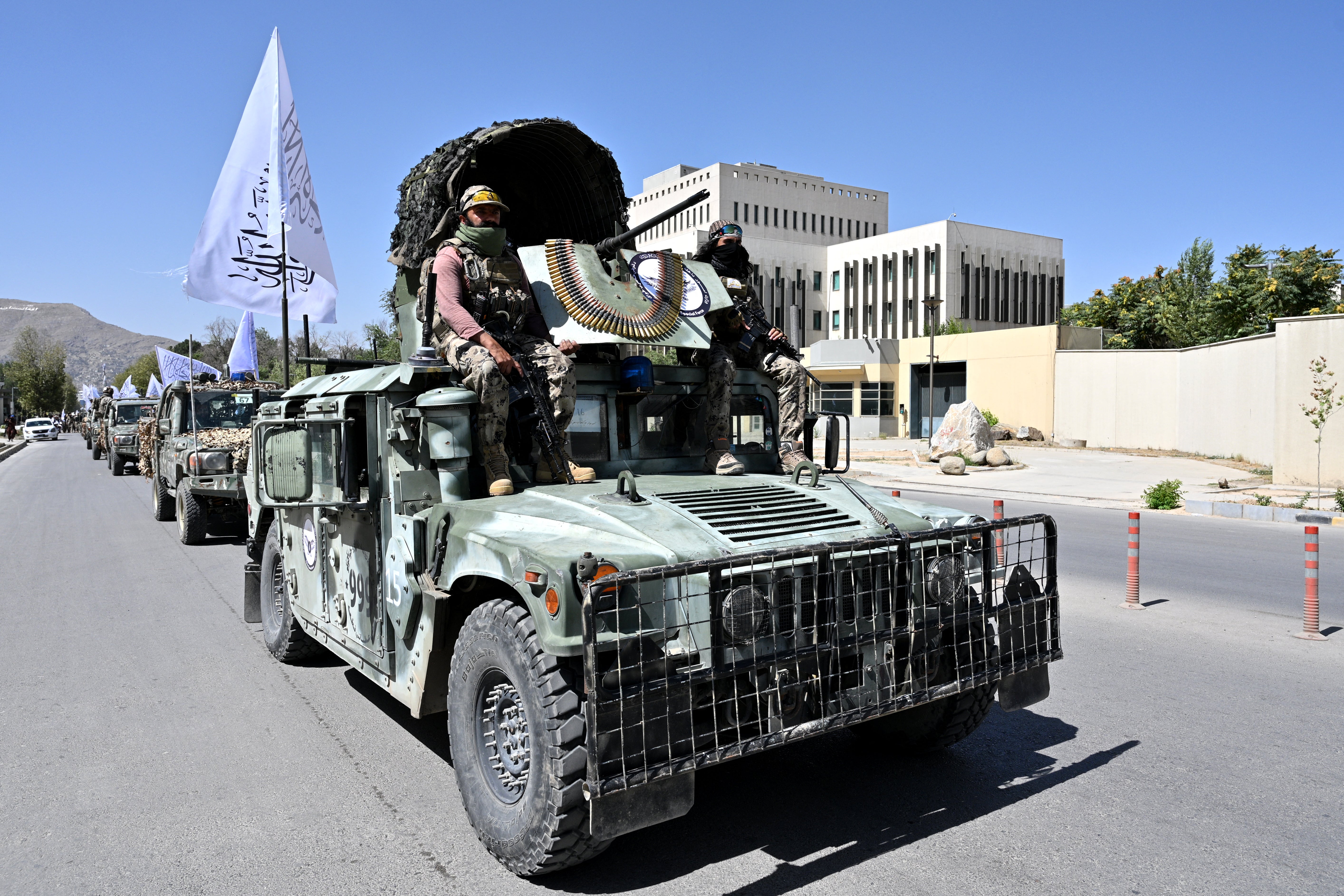A convoy of Taliban security personnel take part in a parade in front of the former US Embassy building (back) in Kabul