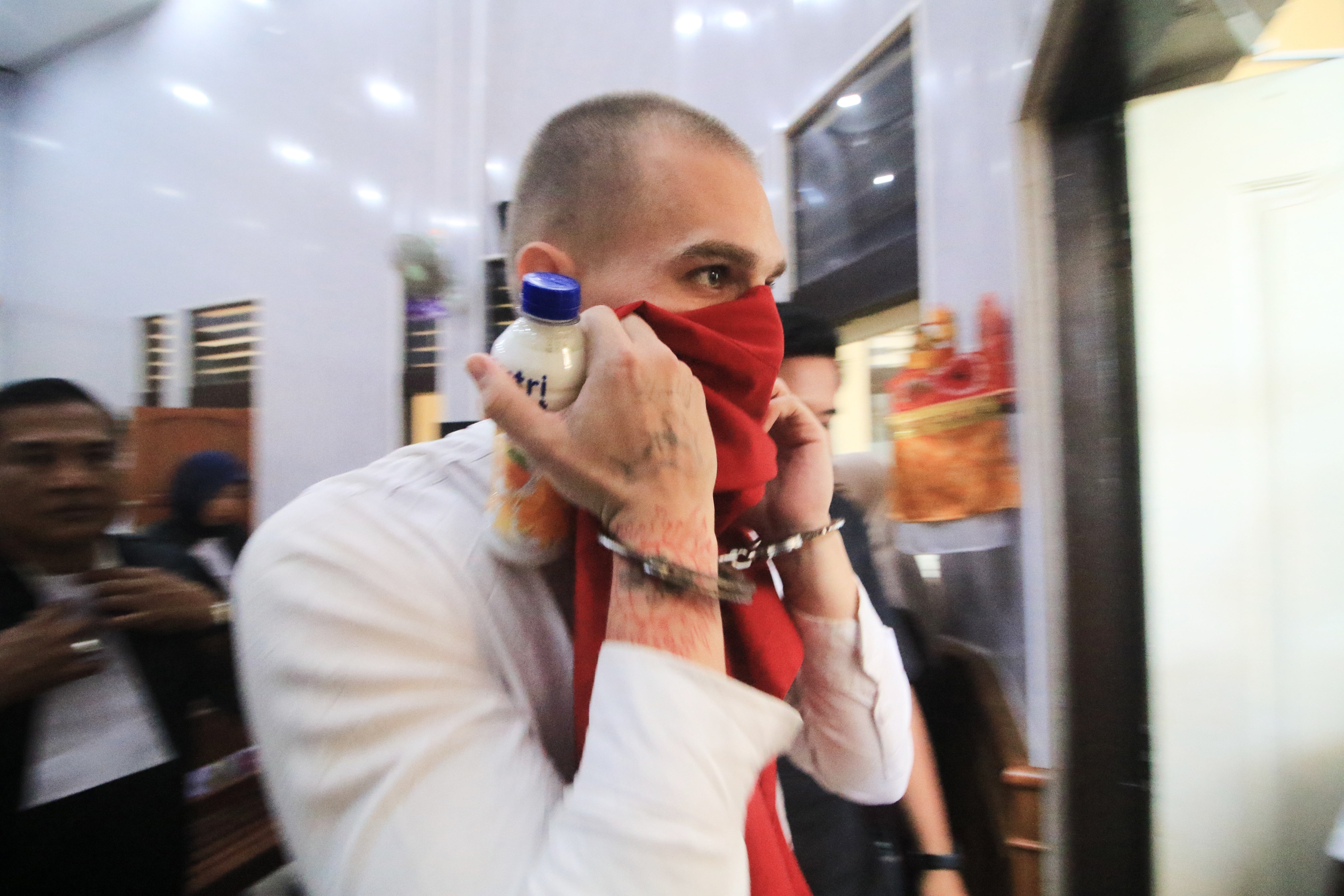 Swiss tourist Luzian Andrin Zgraggen who is accused of insulting the Balinese Hinduism's sacred Day of Silence in social media posts, covers his face as he leaves the courtroom after his sentencing hearing at the district court in Denpasar, Bali, Indonesia