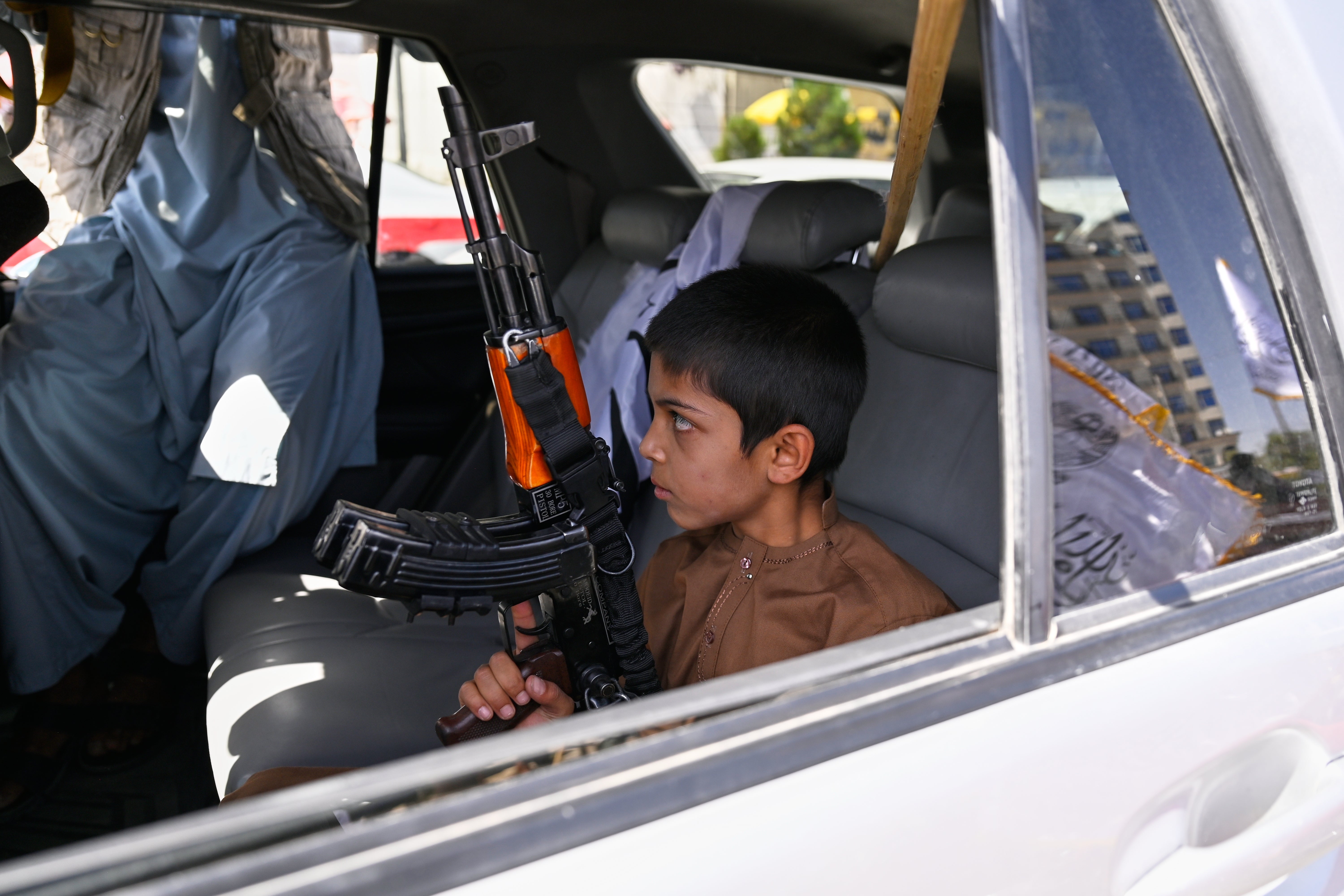 A boy holds an AK-style rifle while sitting in a vehicle decorated with Taliban flags during celebrations marking the fifth anniversary of the US withdrawal from Afghanistan and the Taliban's return to power in Kabul