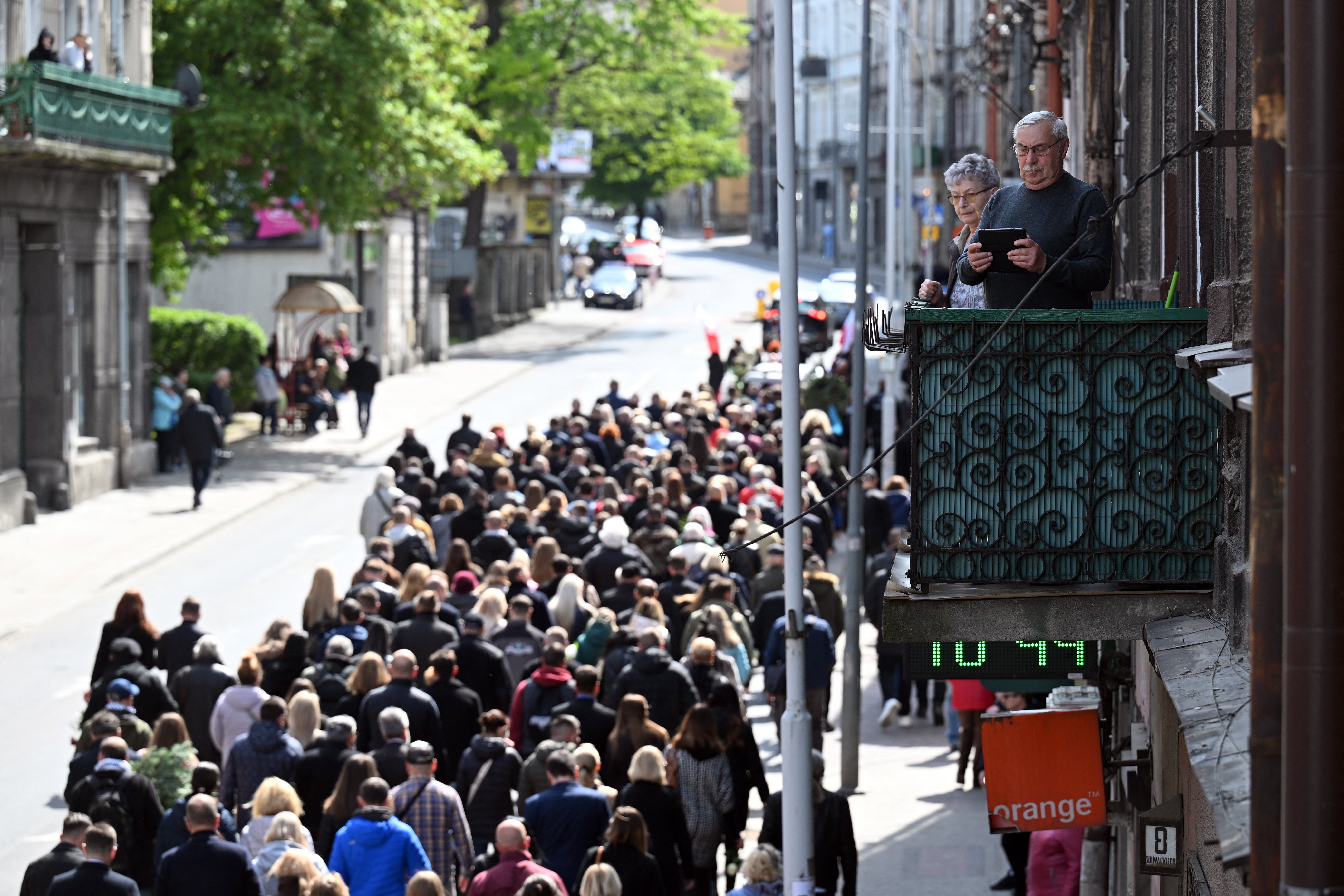 A couple watches from their balcony as mourners attend a funeral procession for Damian Sobol, a member of the US-based food charity World Central Kitchen, killed in an Israeli strike in Gaza, in his home town of Przemysl, Poland, on April 20, 2024