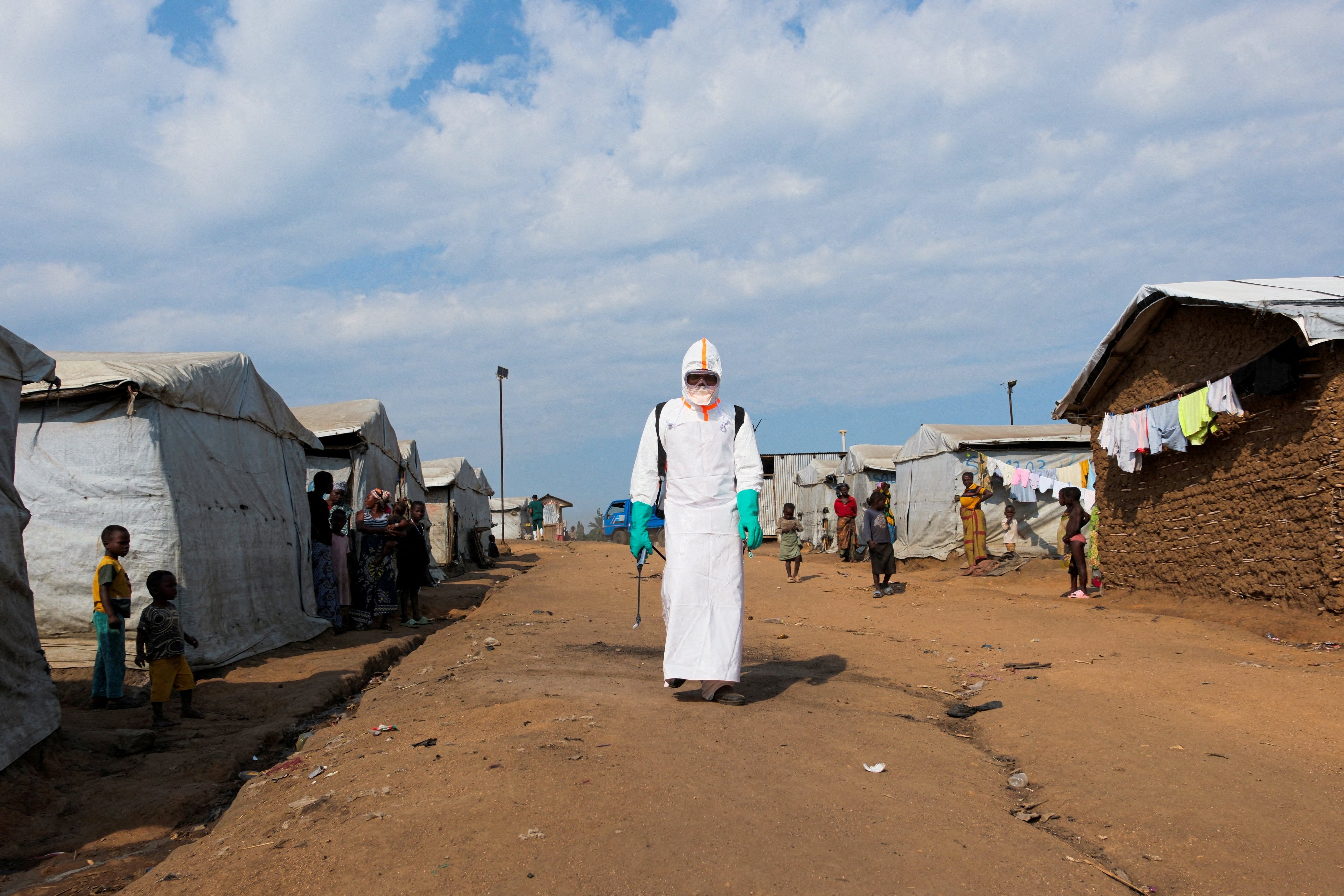 Displaced people watch a health worker in full personal protective equipment (PPE) preparing to disinfect the area during the burial of suspected Ebola victims at the Kigonze displaced persons camp in Bunia, eastern Democratic Republic of Congo