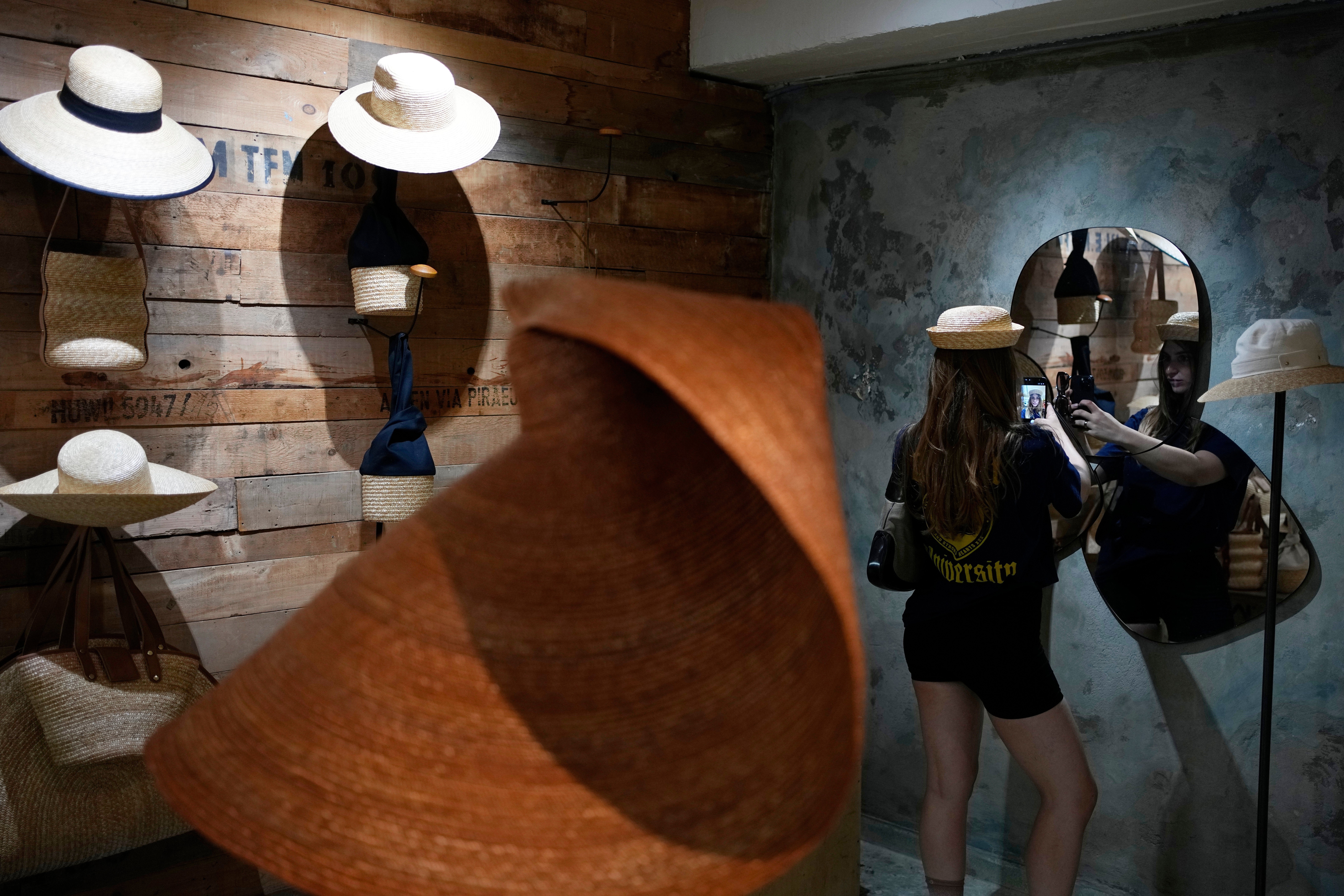 A Russian tourist tries on a hat and takes a selfie at a shop in Athens, Greece, Tuesday, Aug. 11, 2026. (AP Photo/Thanassis Stavrakis)