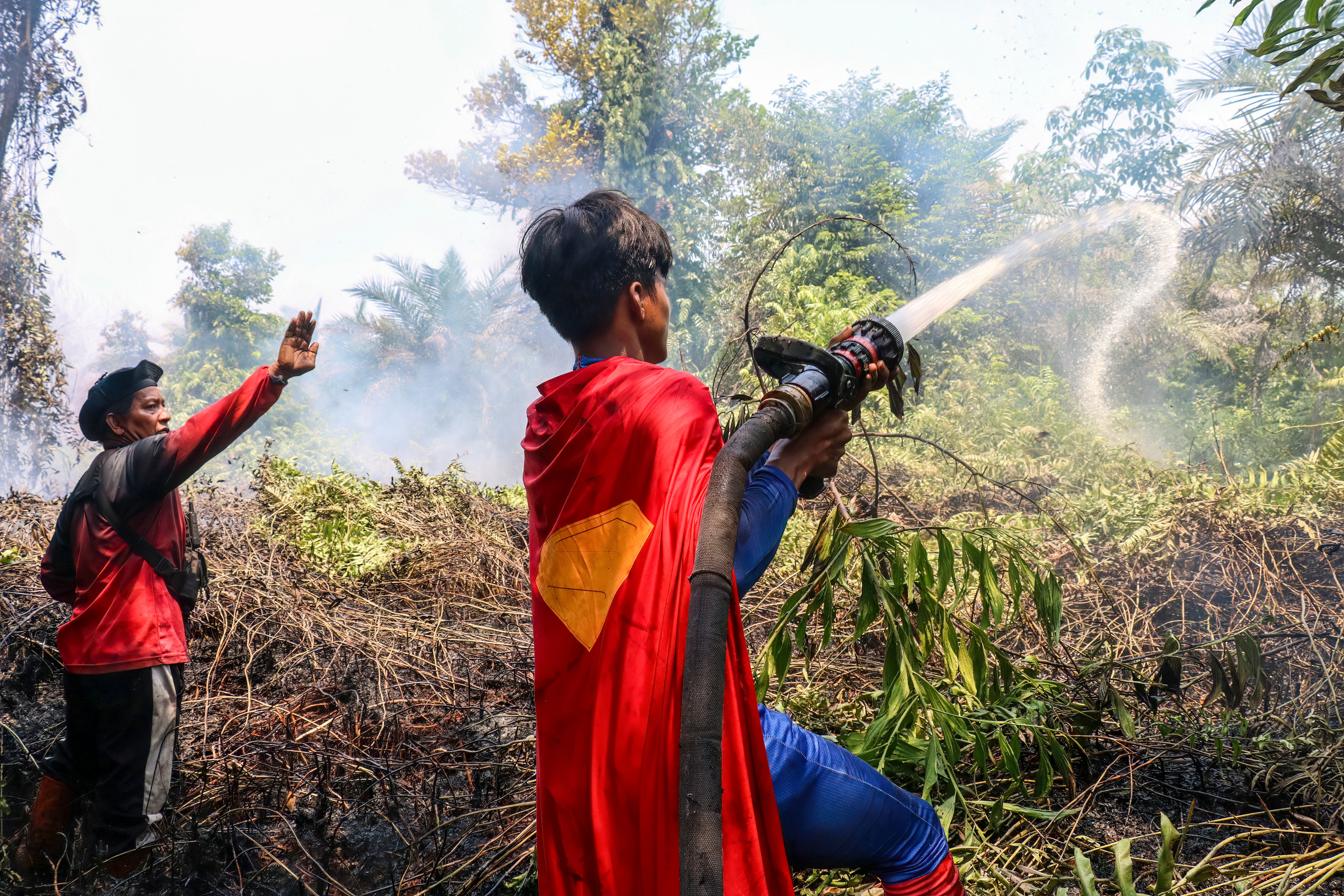Indonesian student Rudiansyah (R) dressed in a Superman costume helps to extinguish a forest and land fire at Petuk Katimpun in Palangka Raya, Central Kalimantan, on 17 August 2026