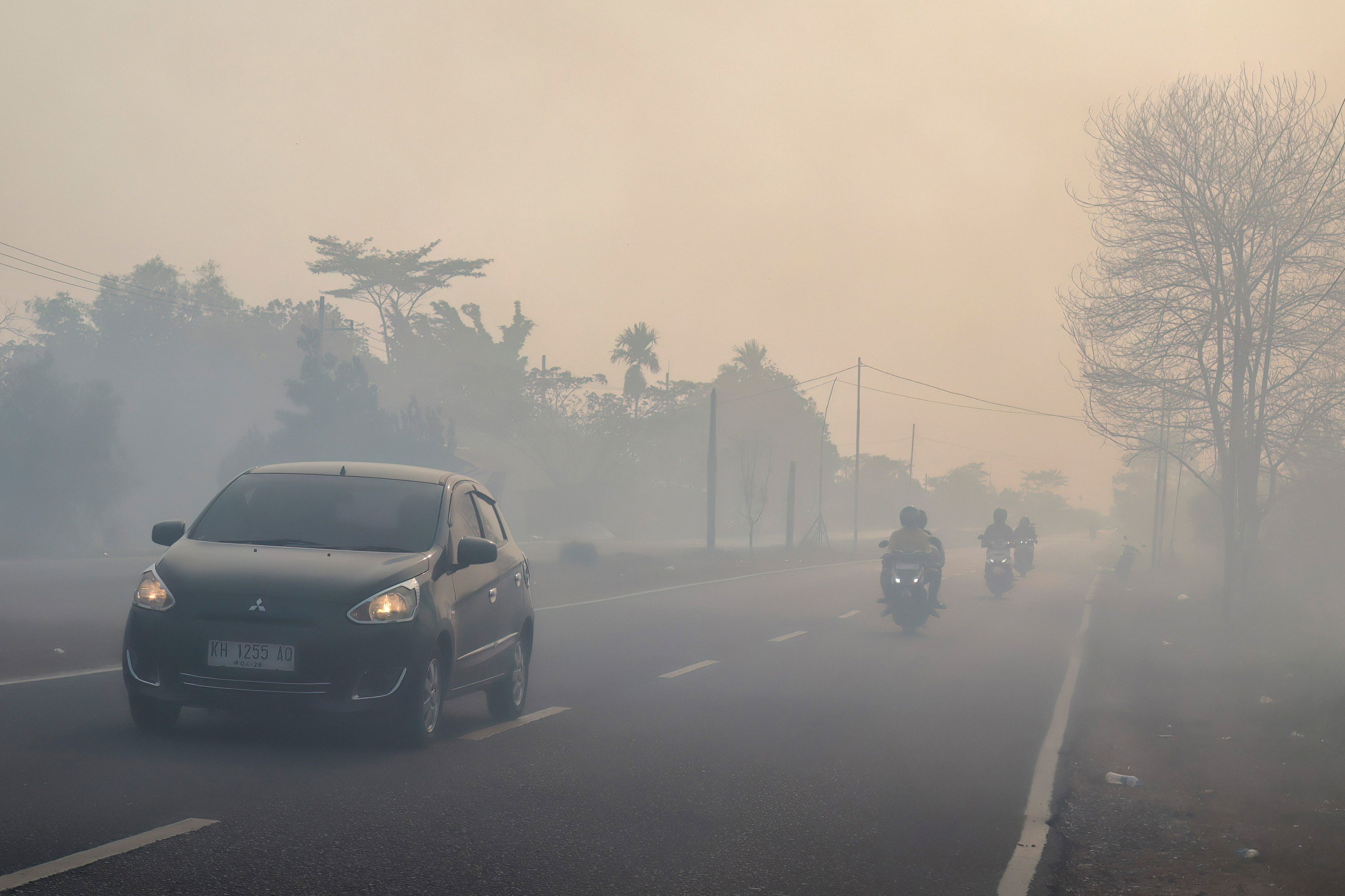 Motorists drive with headlights on a haze-shrouded road in Palangkaraya city, central Kalimantan on 20 August 2026, as smoke originating from widespread forest and land fires has significantly reduced visibility and degraded air quality across the province