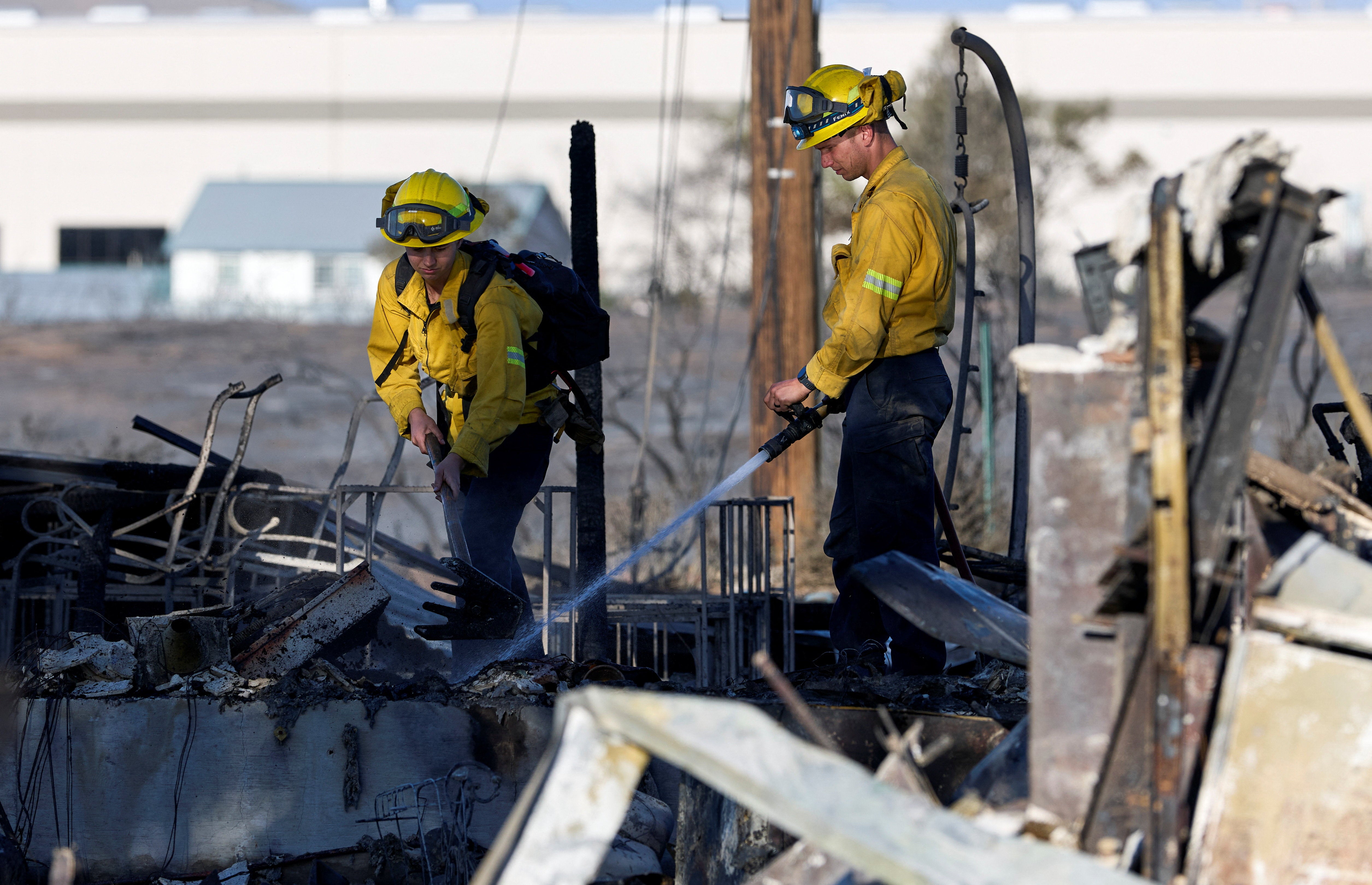 Two firefighters knock down hotspots in the charred remains of a home burned