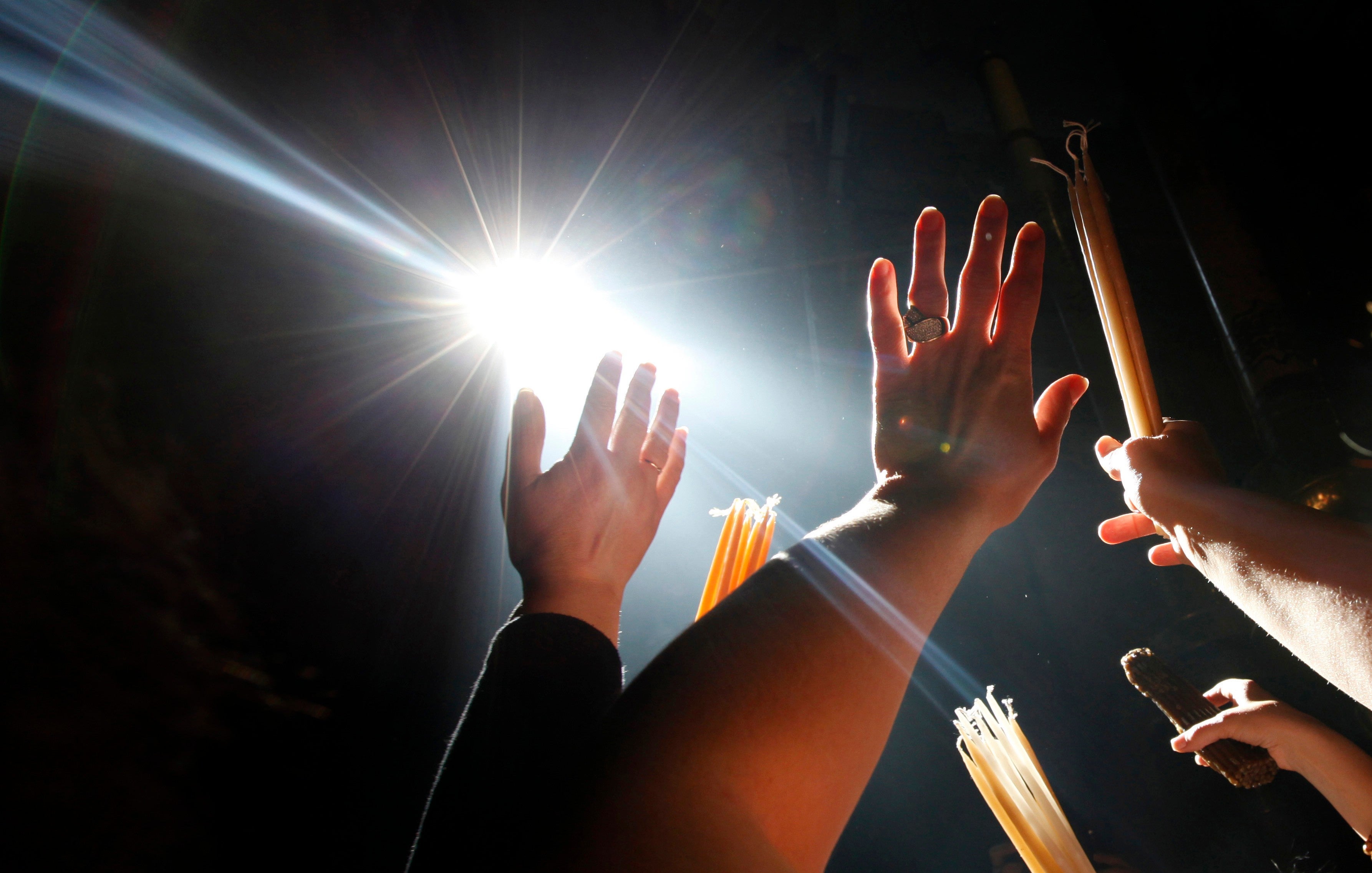 Christian Orthodox pilgrims raise their hands towards a beam of light in front of the Edicule at the Church of the Holy Sepulcher