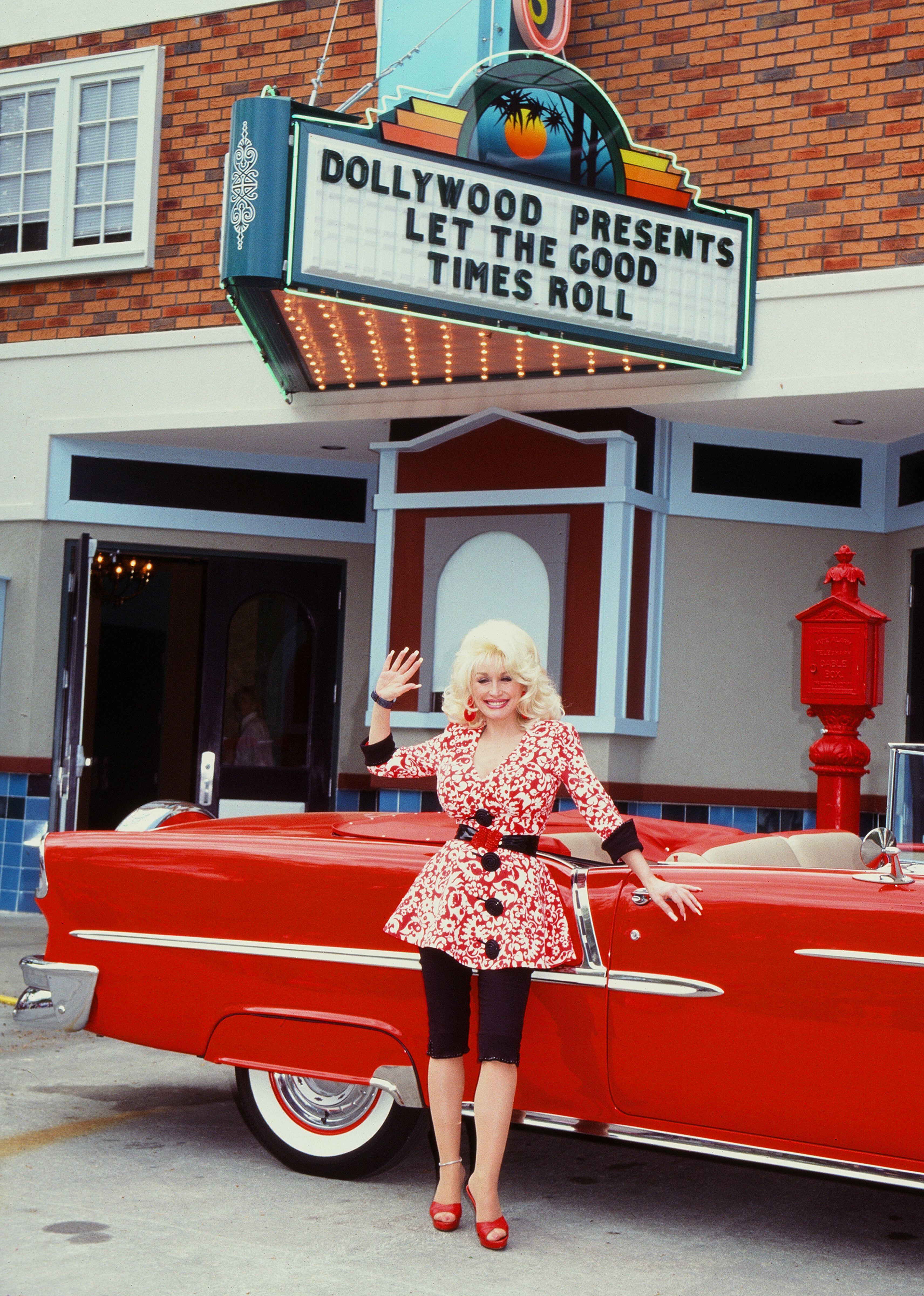 Standing beside a cherry red Fifties convertible beneath a Dollywood sign, Parton almost appears dressed as an extension of her own brand (Alamy/PA)