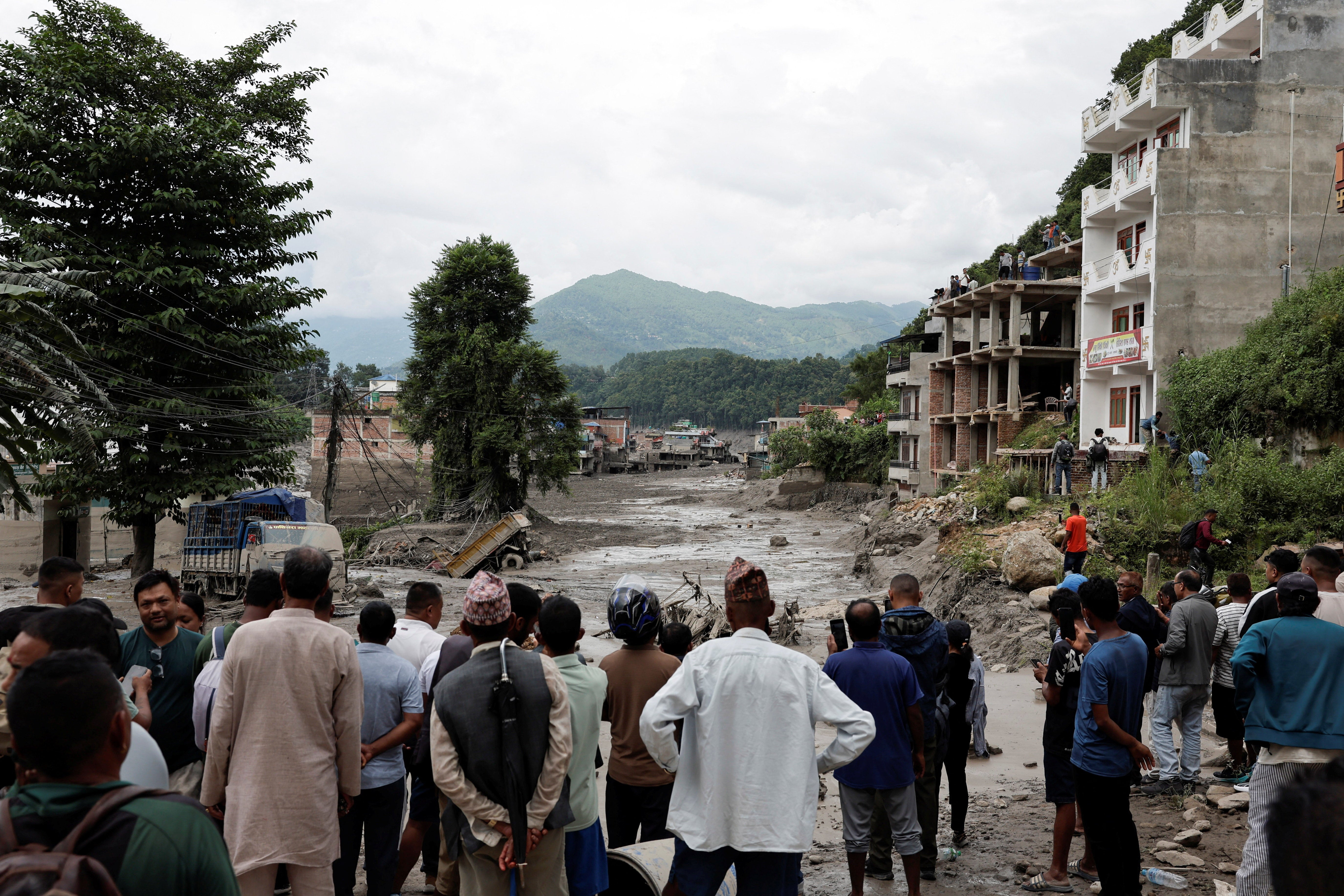 People stand near mud covered houses and a road, following a flash flood at Trishuli (Reuters)