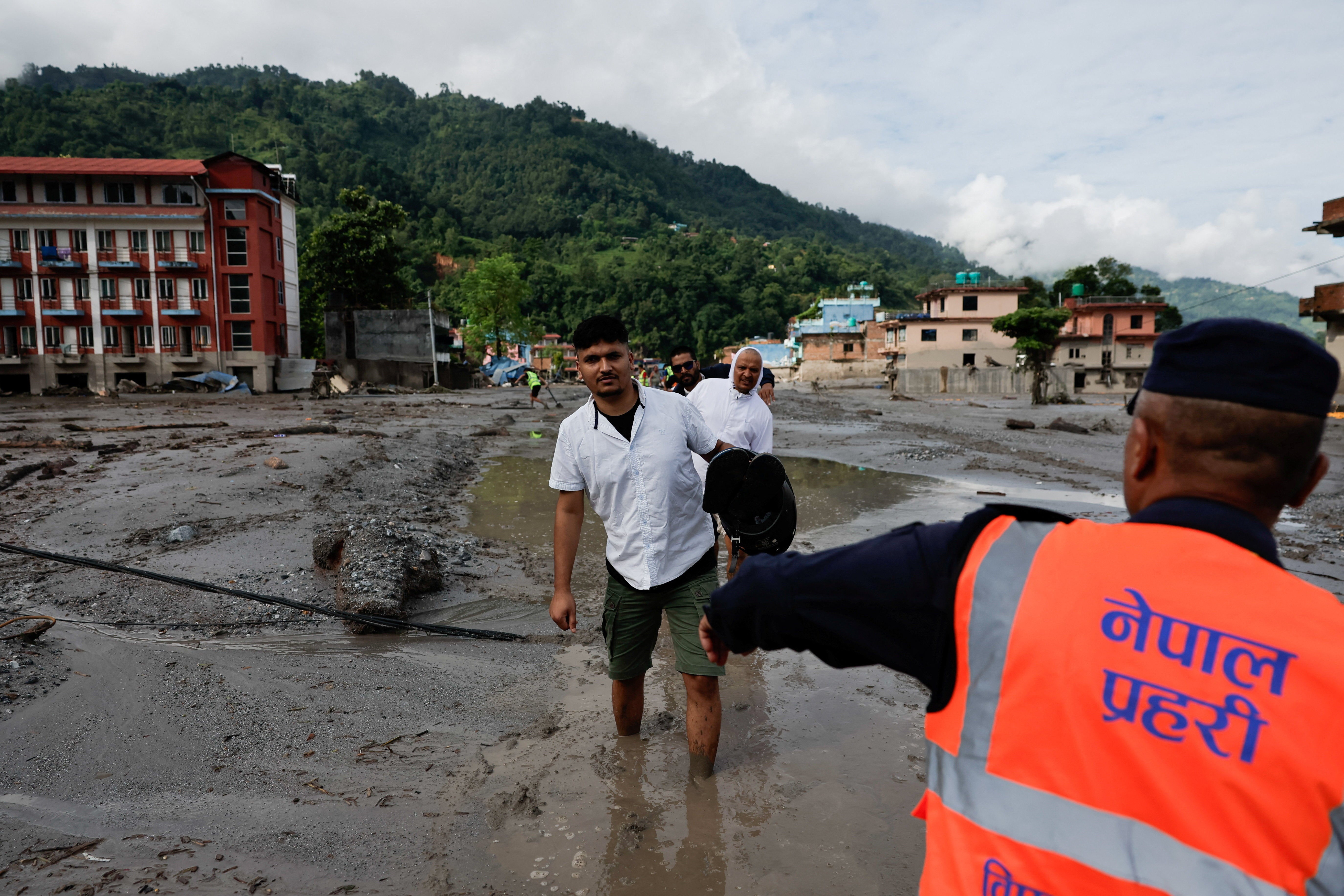 People wade through muddy waters following devastating floods, in Trishuli in Nuwakot district, Nepal, August 27, 2026