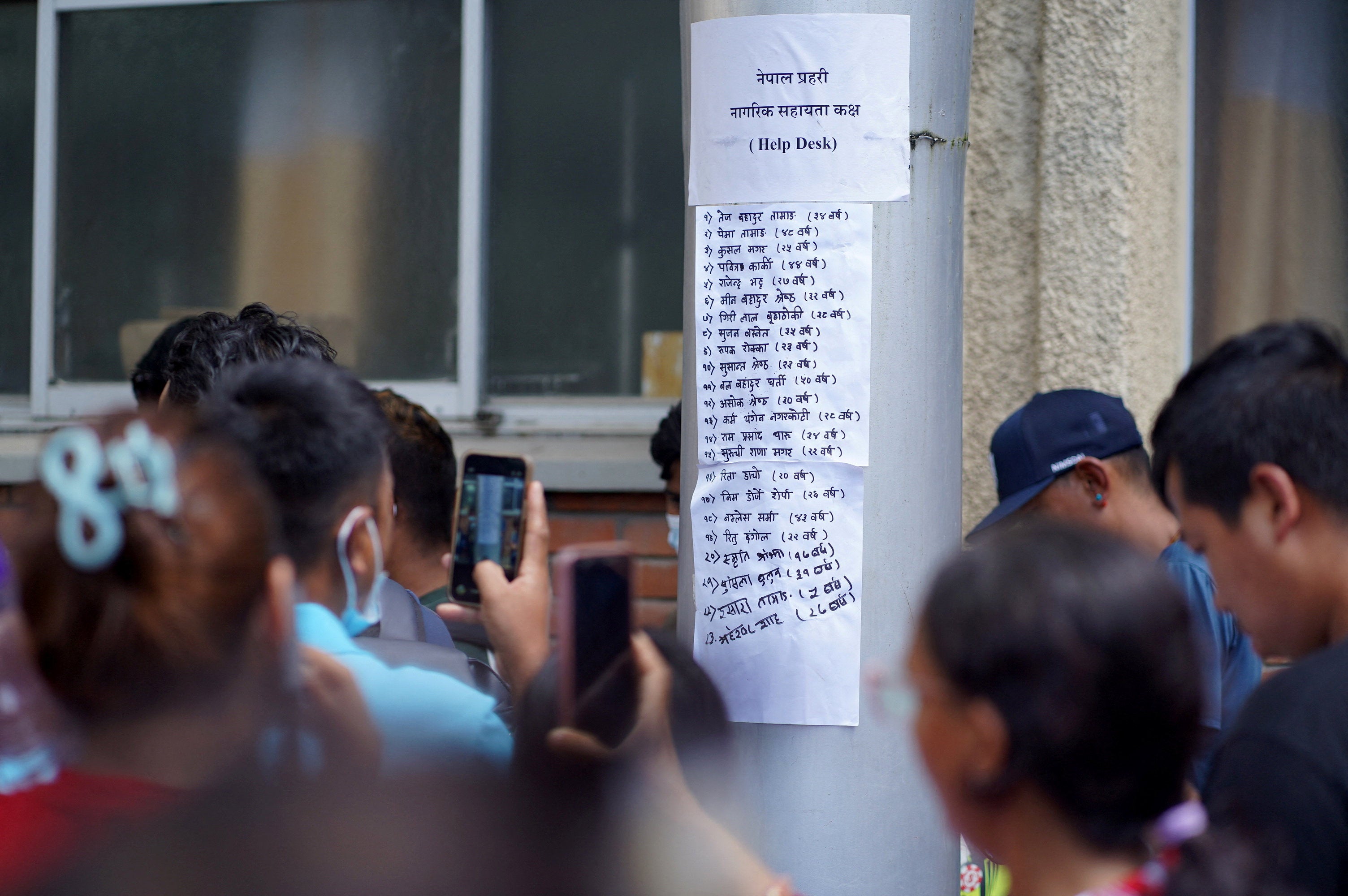 People use their mobile phones to film a list of injured people pasted on a hospital wall following deadly floods in Kathmandu, Nepal, 27 August 2026