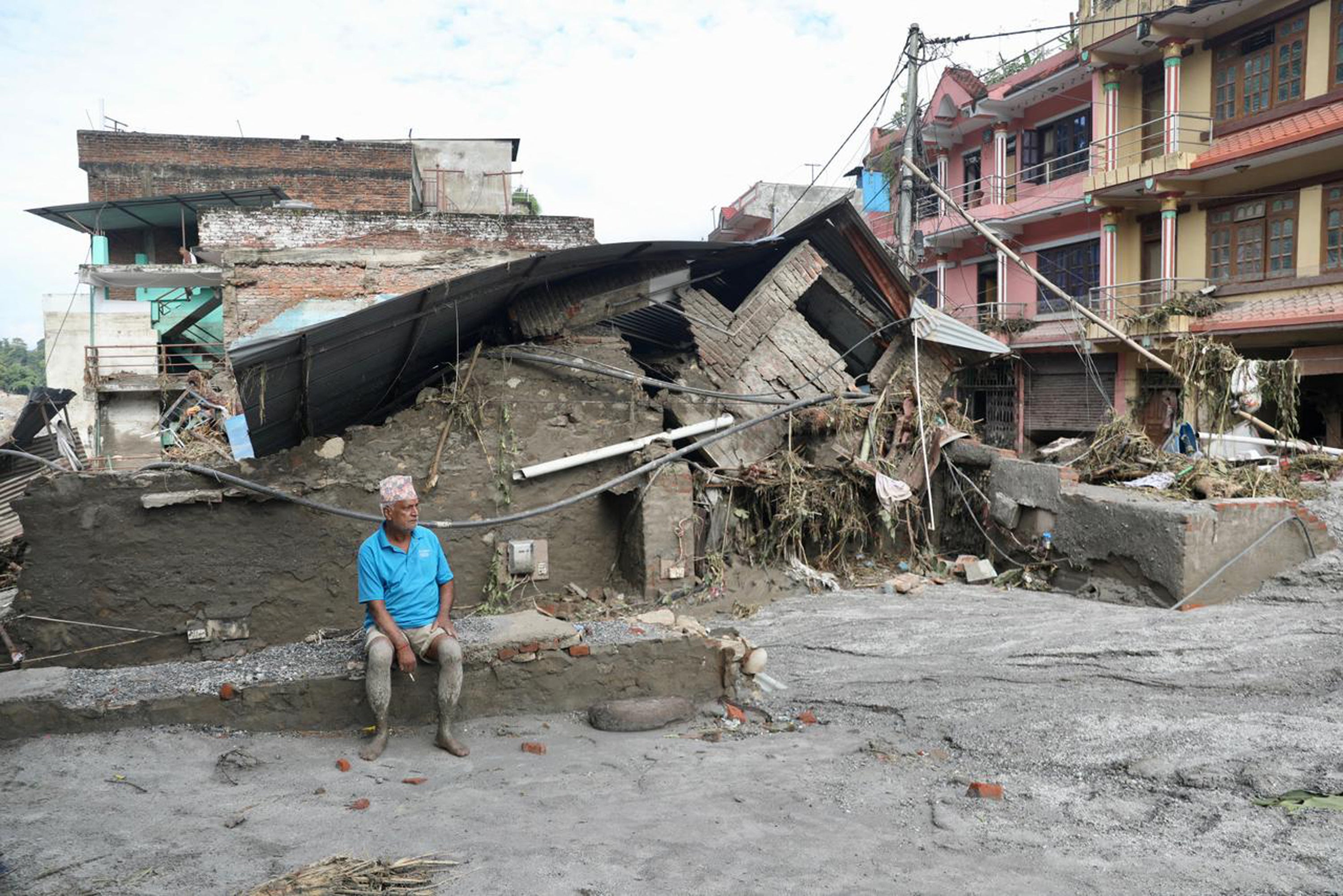 A resident sits near a collapsed house lying deluged in sludge after flash floods at Devighat, Bidur Municipality in Nepal’s Nuwakot district