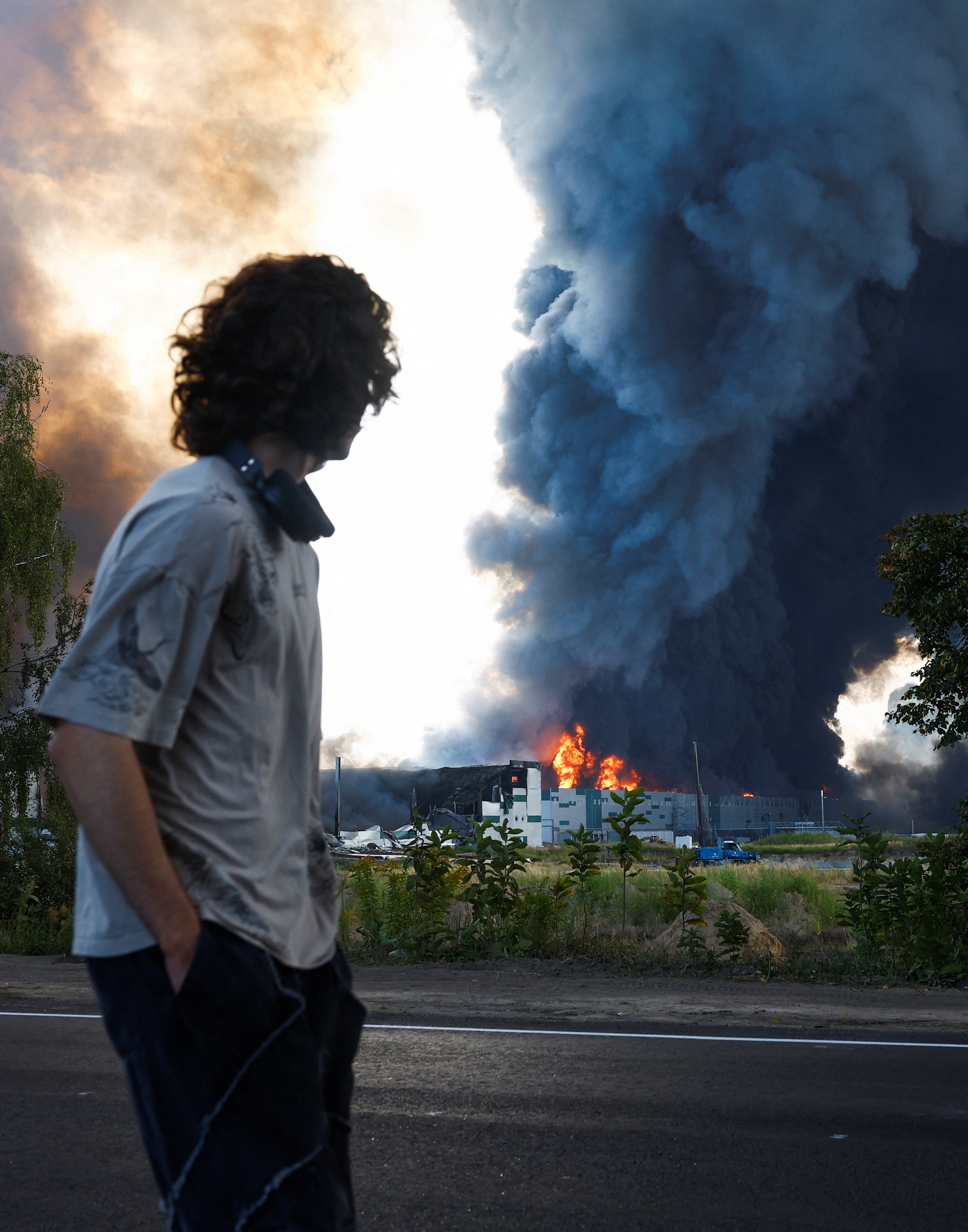 A man looks on as smoke rises over a warehouse, which was hit by a Russian drone strike, amid Russia's attack on Ukraine, in Kyiv region, Ukraine, August 27, 2026.