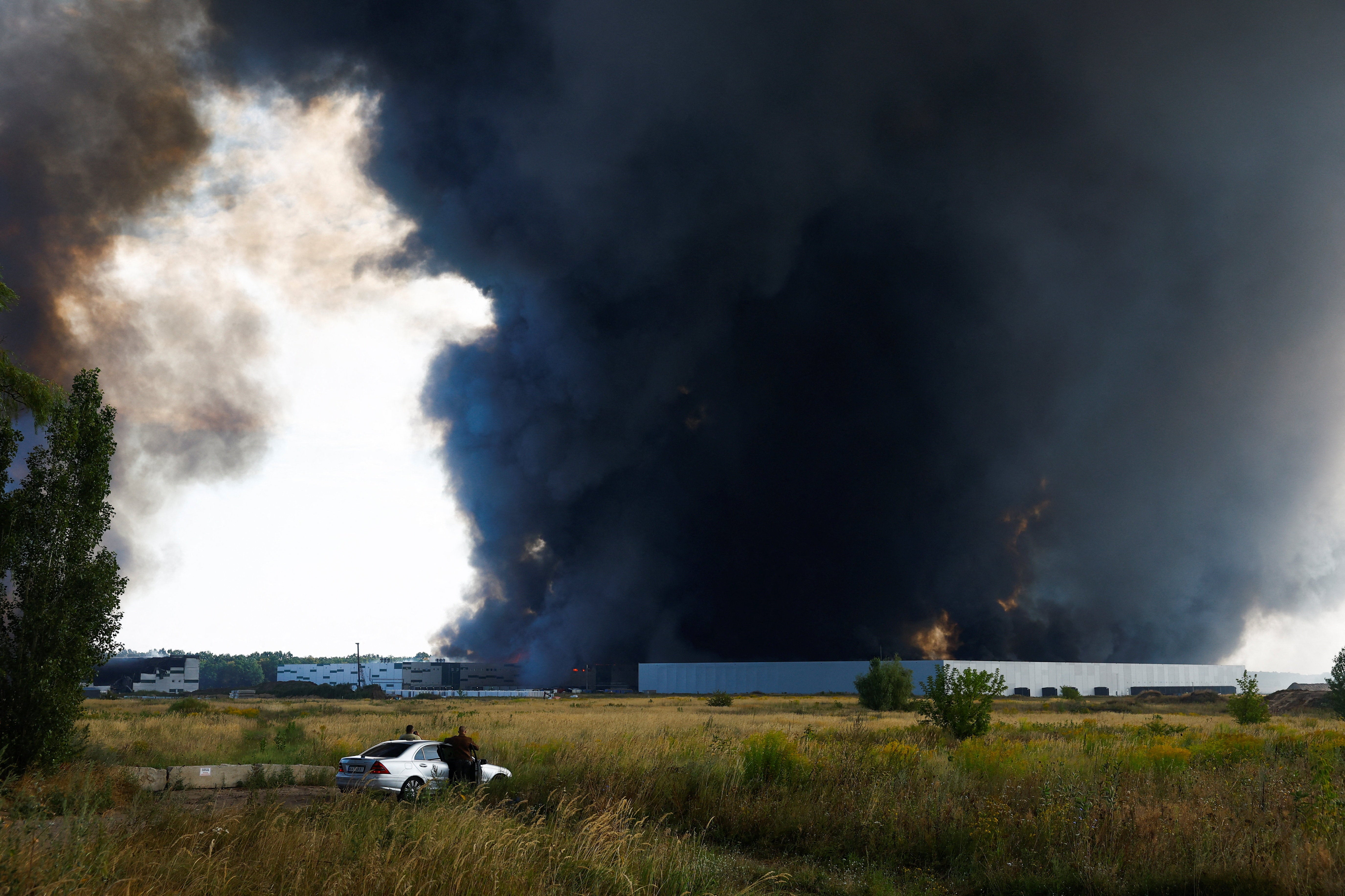 People watch as smoke rises over a warehouse, which was hit by a Russian drone strike, amid Russia's attack on Ukraine, in Kyiv region, Ukraine, August 27, 2026.