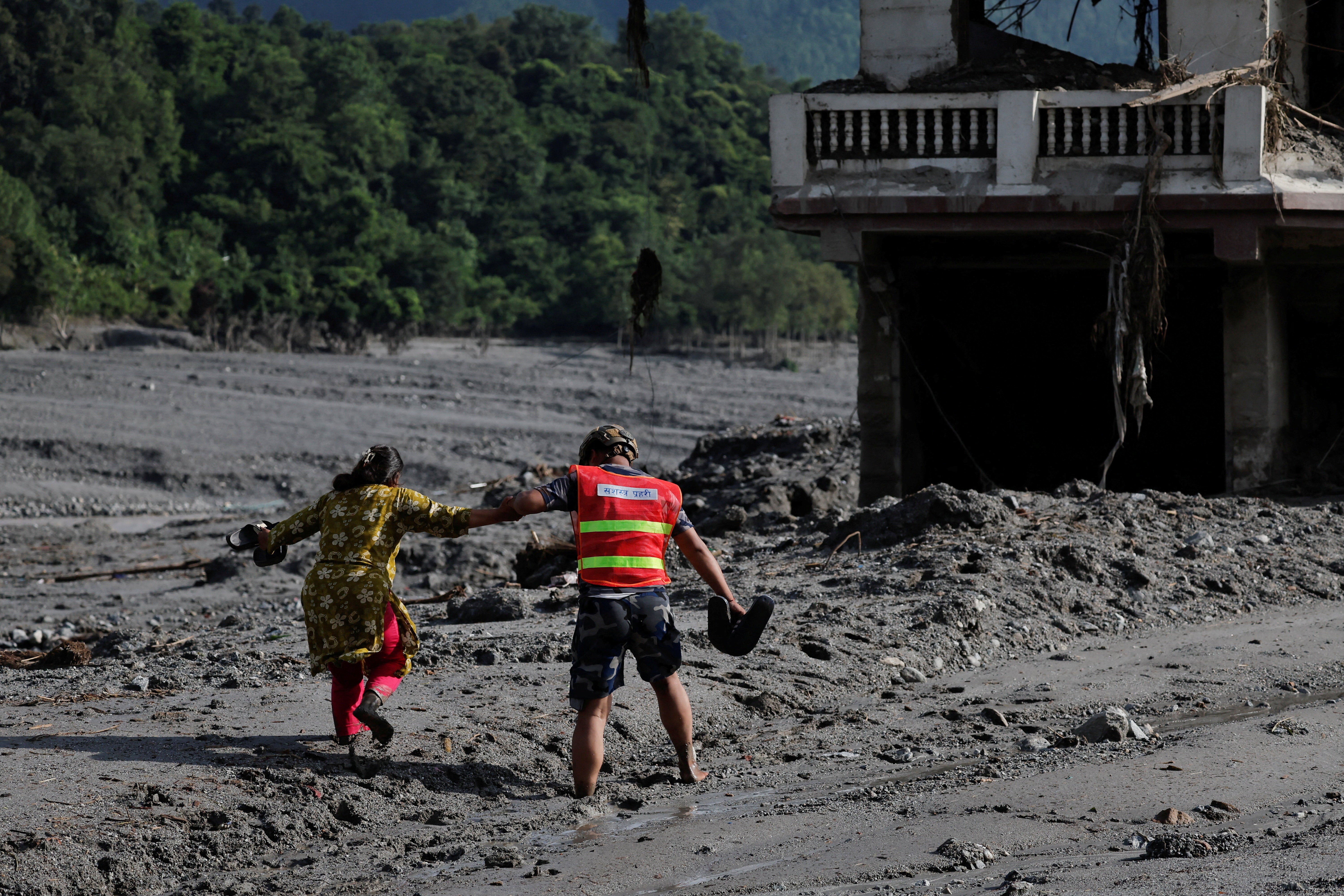 A rescue worker helps a woman move through a muddy road following flash floods and a mudslide in Trishuli, Nepal, on 28 August 2026 (Reuters)