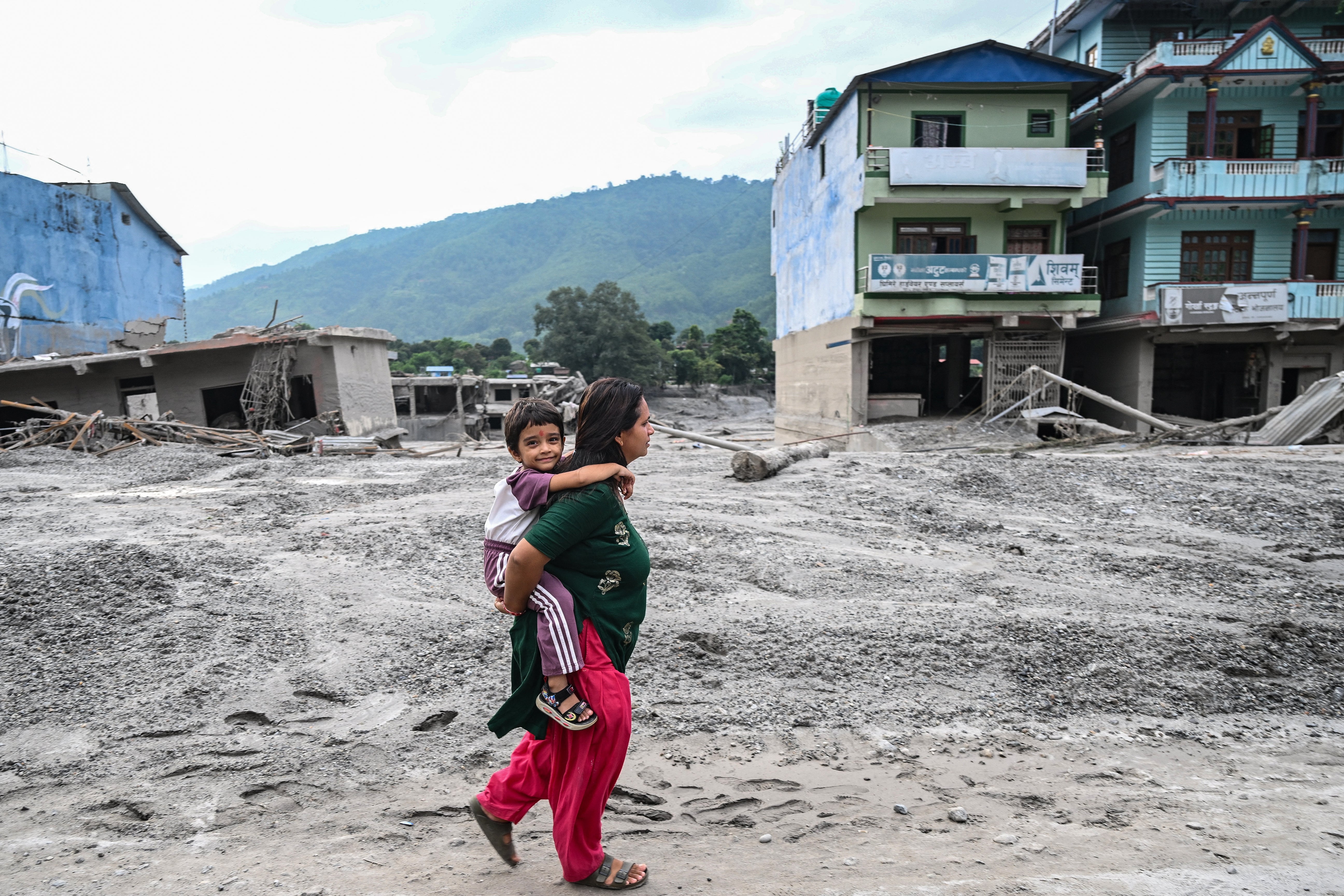 A woman carrying her child walks along a road deluged in sludge after flash floods at Devighat in Nepal's Nuwakot district