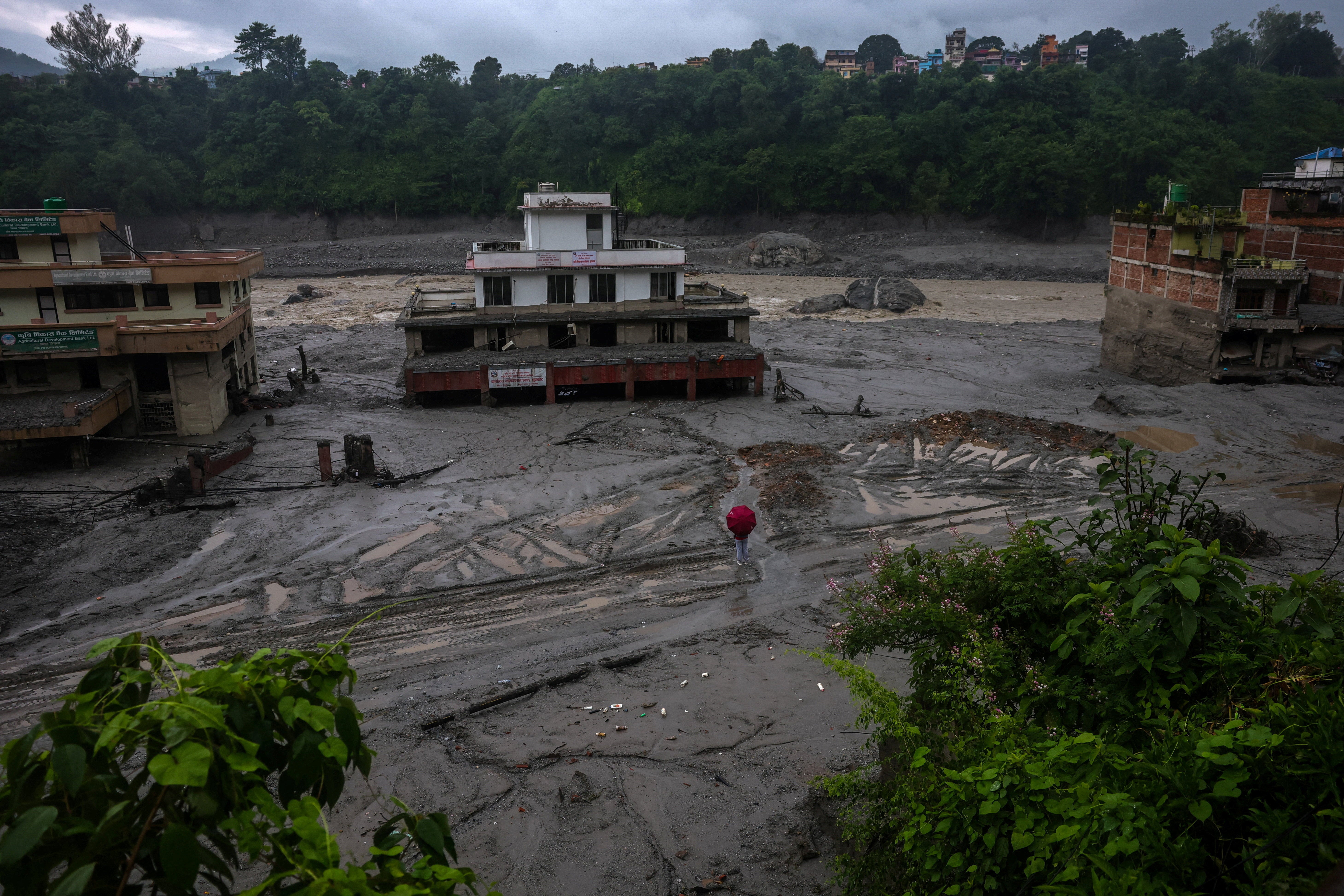 A person holds an umbrella as he stands in front of damaged buildings after flash floods and a mudslide, in Trishuli, Nuwakot district, Nepal