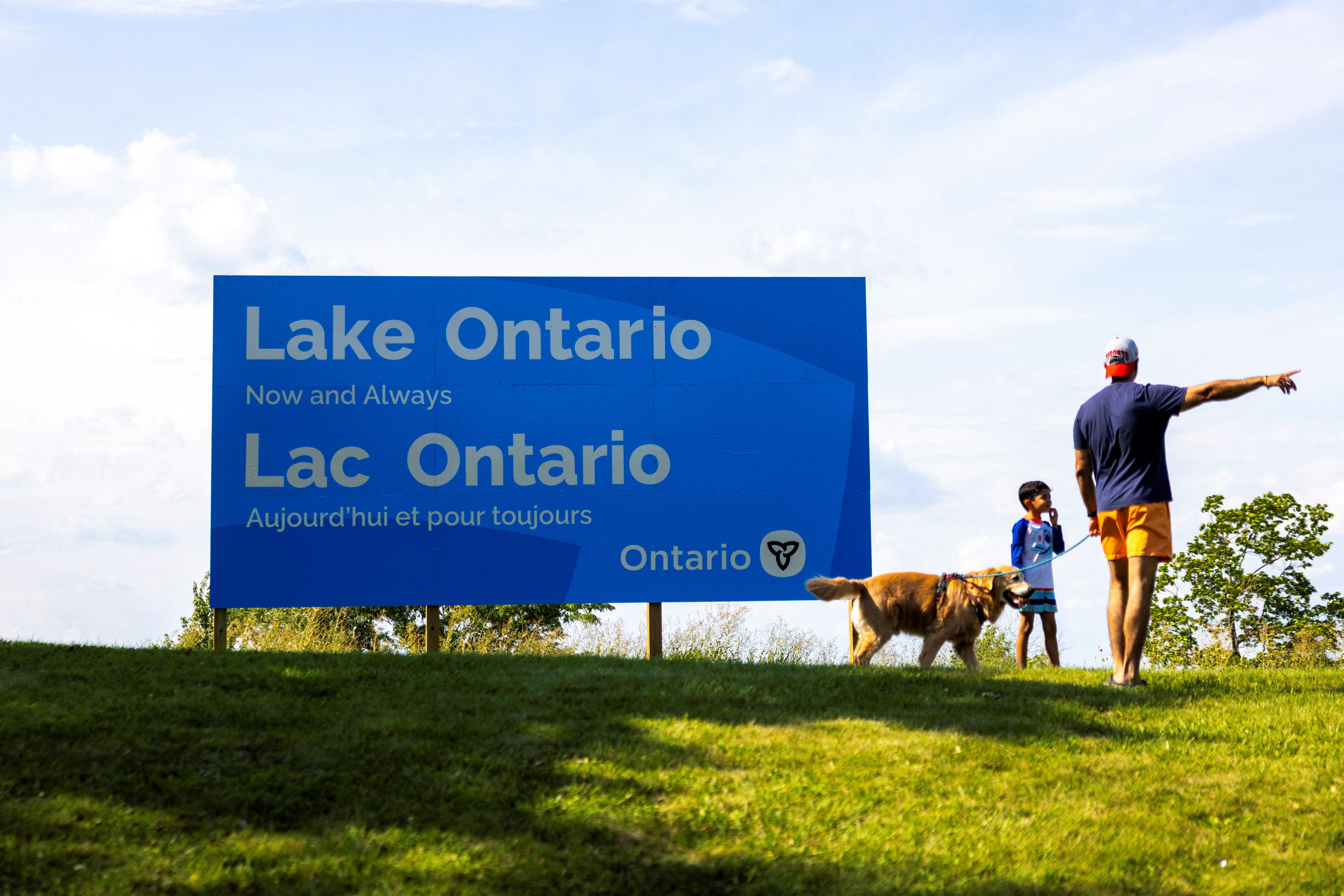 A family walks by a sign reading "Lake Ontario, Now and Always"