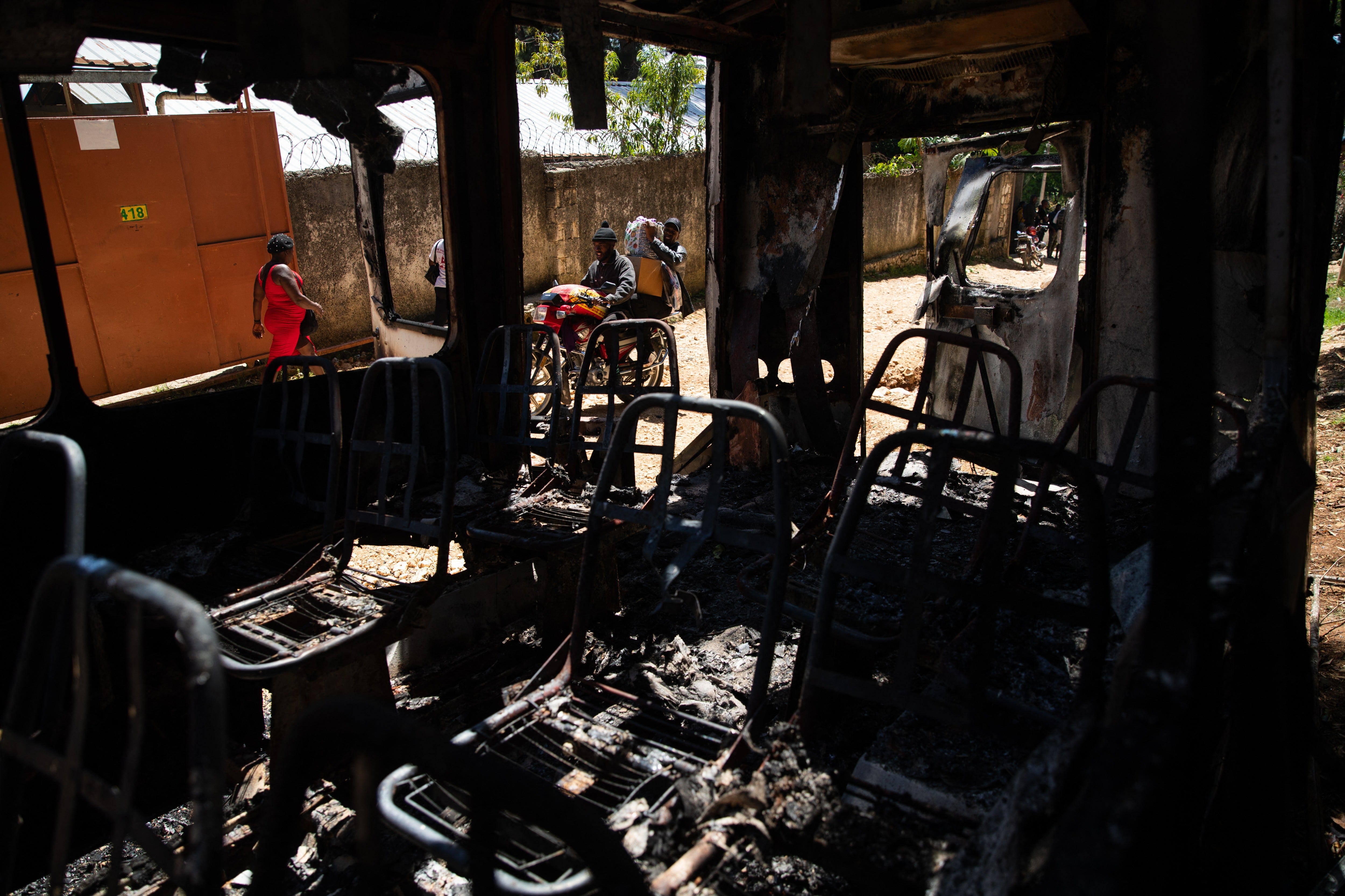 Pictured: People walk past the remains of a charred vehicle following overnight violence in Kenscoff, a neighborhood near Port-au-Prince, Haiti, on August 24