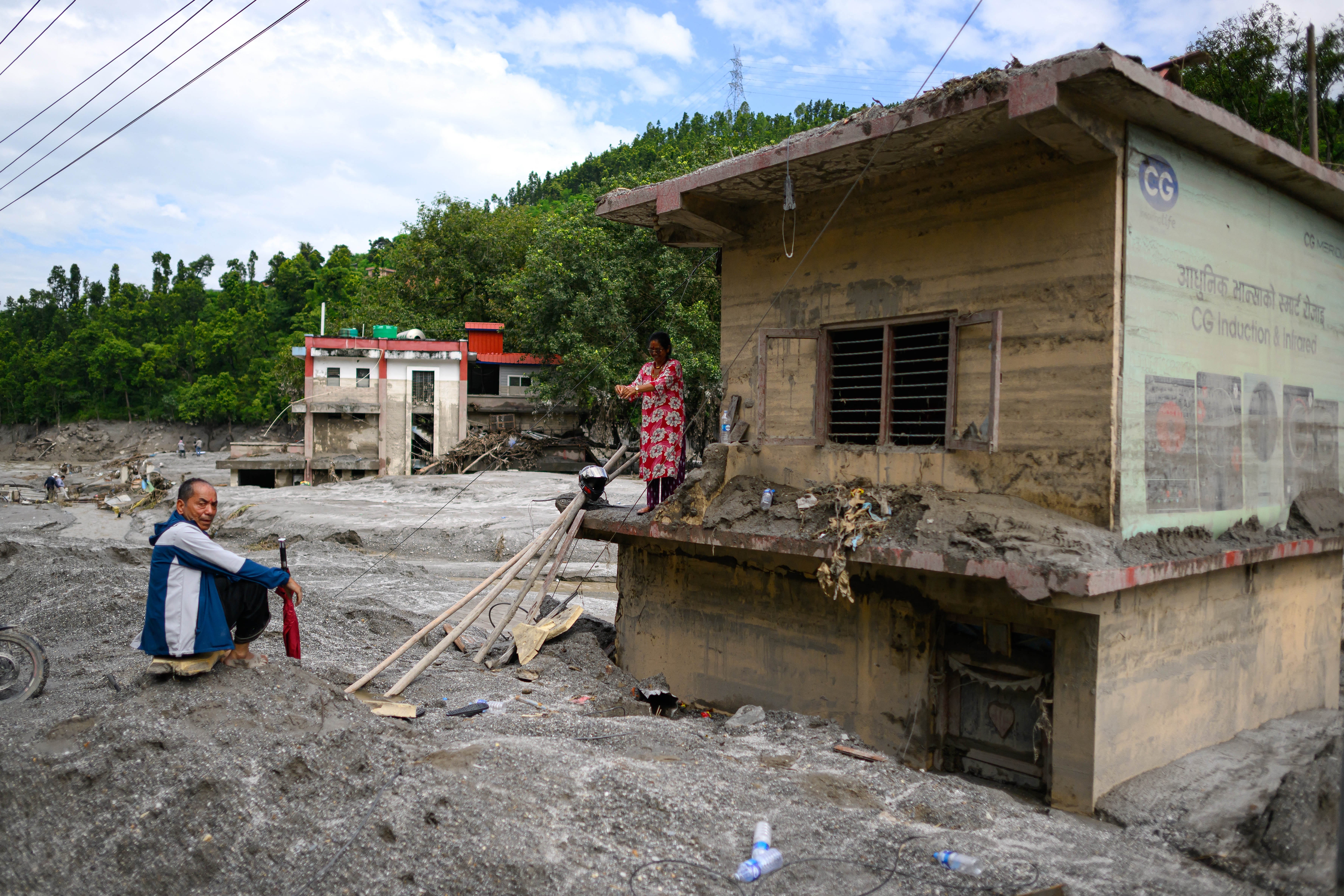 A woman (R) stands atop her house covered in mud in the aftermath of flash floods at Baireni in Nepal's Dhading district on 30 August 2026