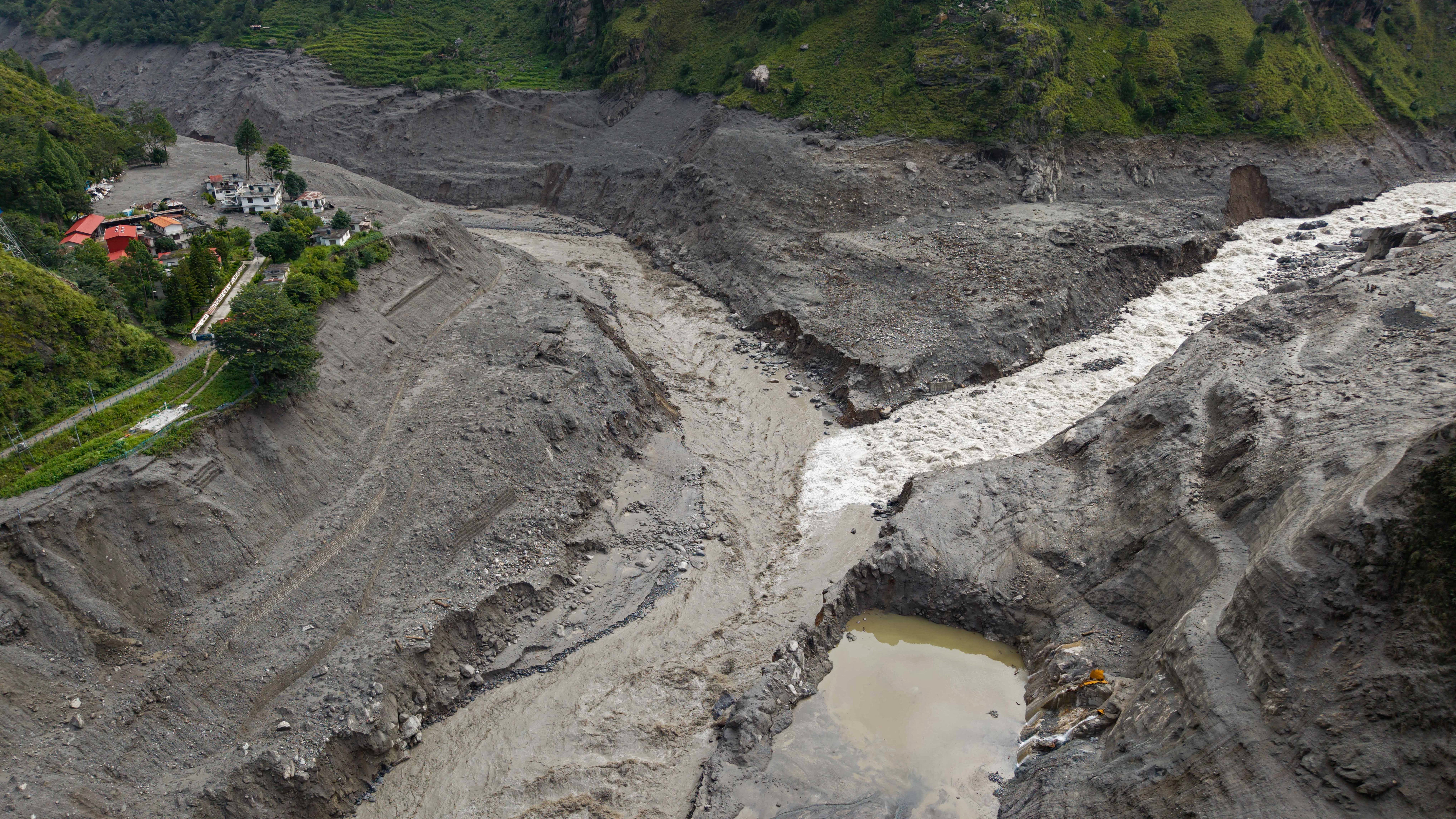 An aerial view shows a torrent of muddy water surging past houses and through the Trishuli River in the aftermath of flash floods