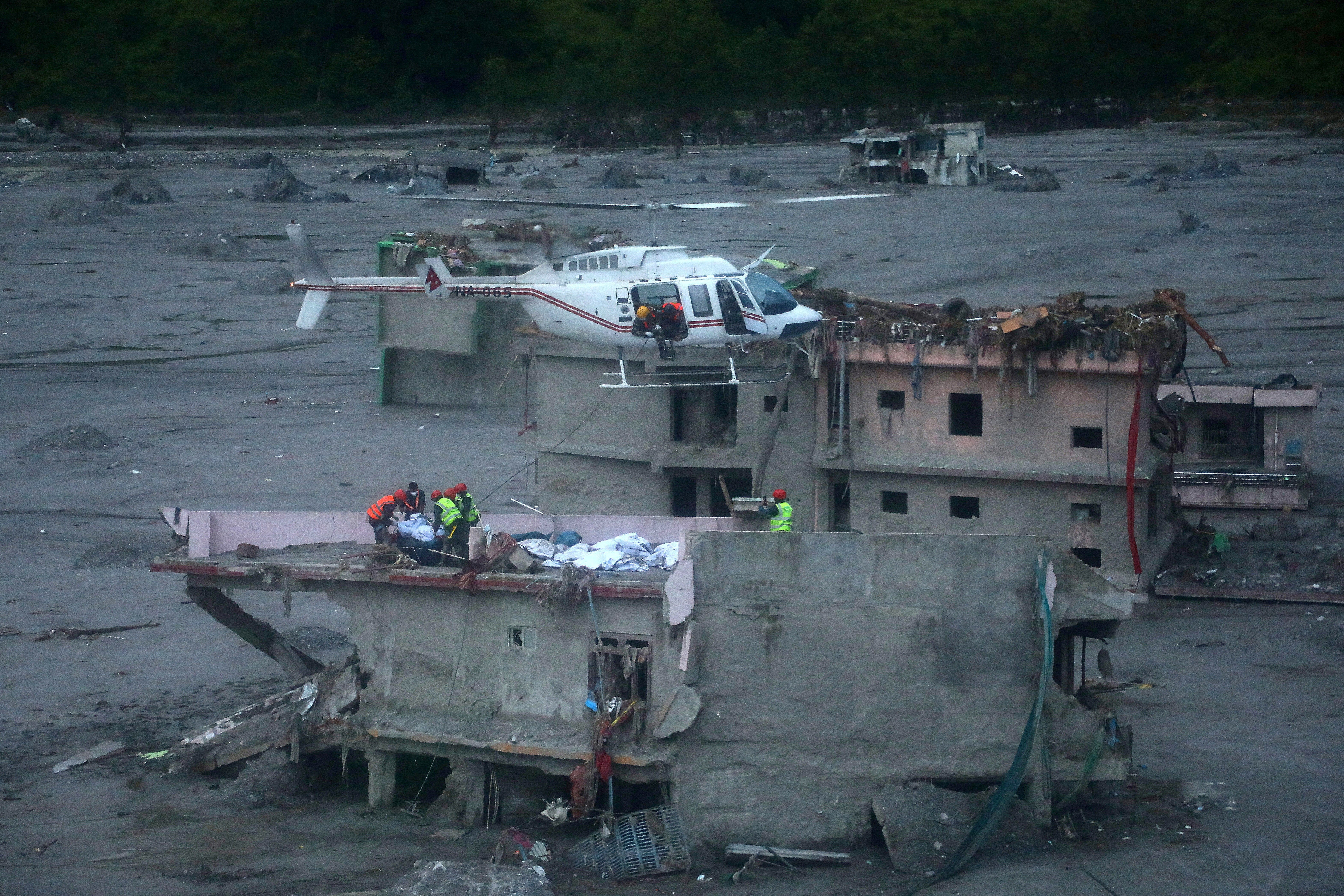 Rescuers prepare to lift the body of a flood victim from the roof of a damaged house in Betrawati Bazaar, Nepal