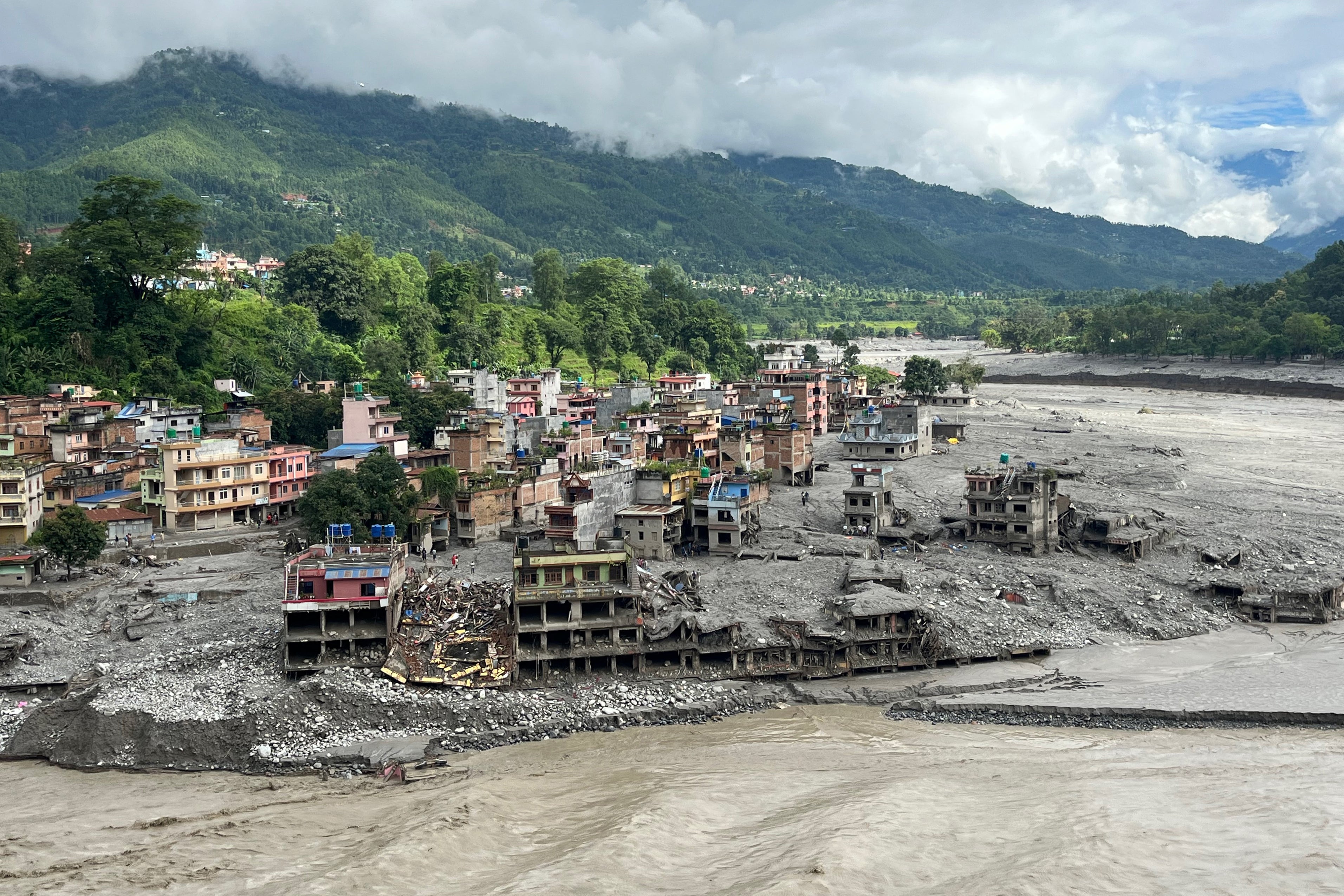 An aerial view shows a torrent of muddy water surging past houses and through the Trishuli River in the aftermath of flash floods at Trishuli Center in Nepal's Nuwakot district