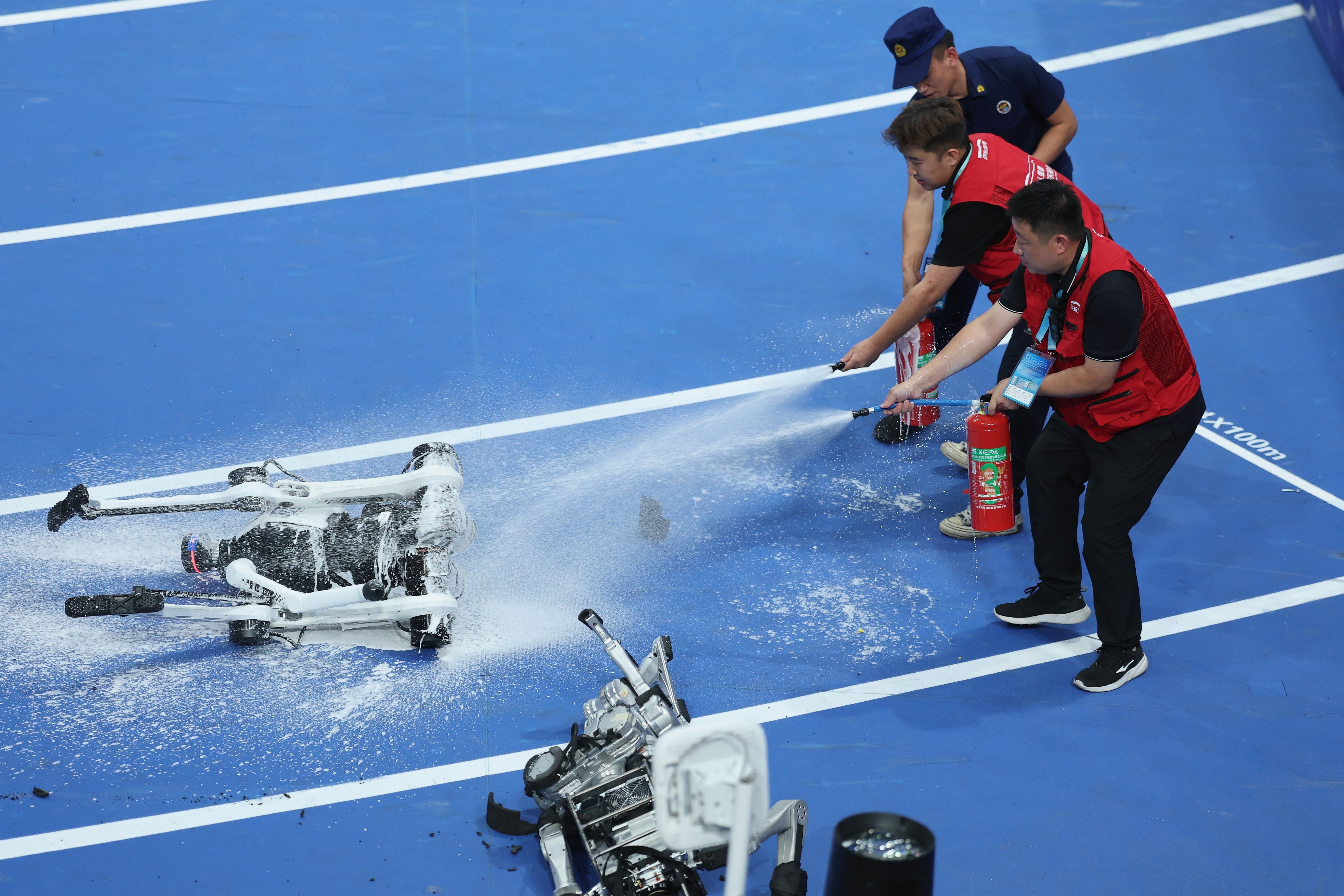 Humans spray a humanoid robot with a fire extinguisher after it fell and caught fire upon crossing the finish line at the World Robot Games