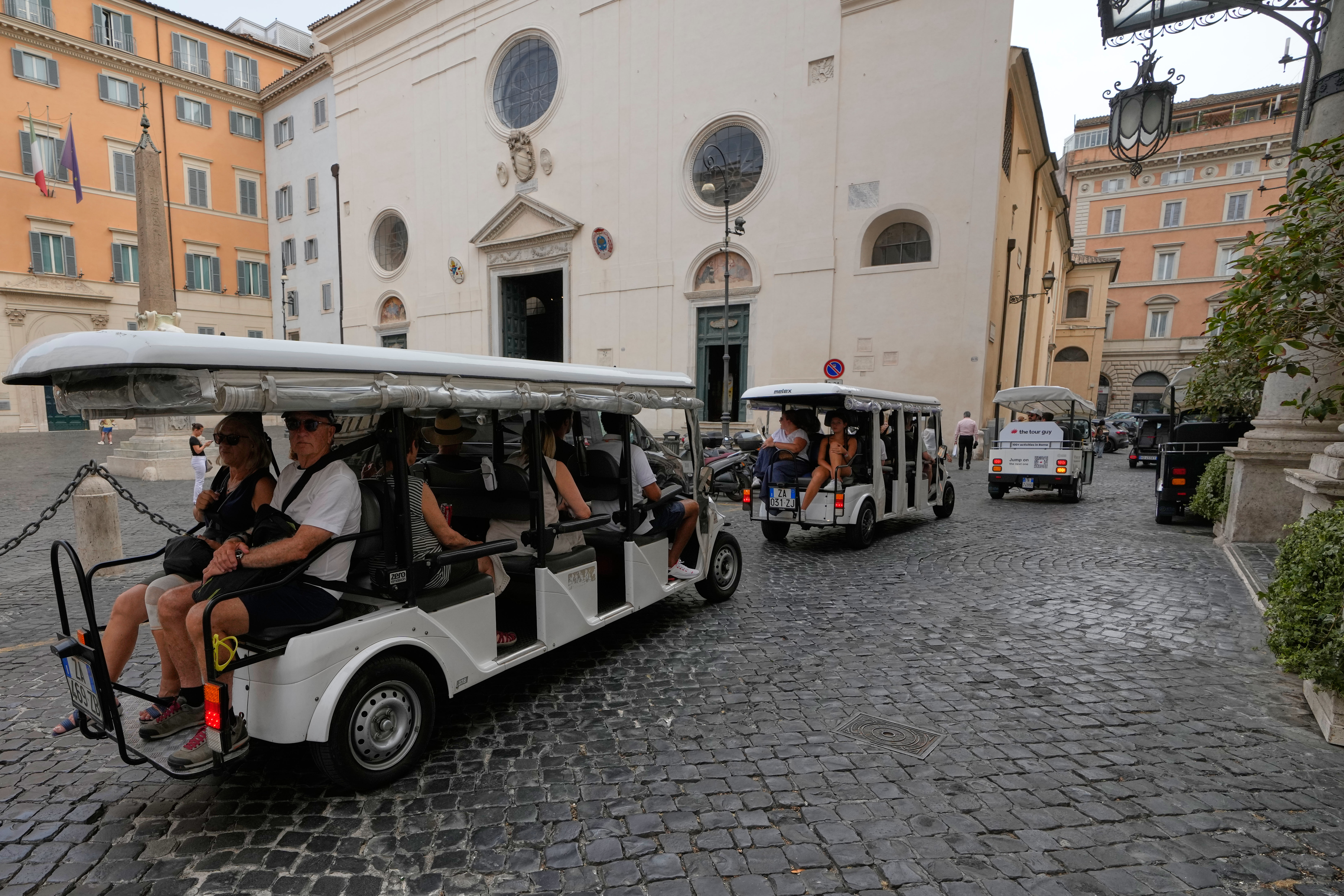 A flotilla of golf carts carrying tourists travels past the Basilica of Santa Maria sopra Minerva in Rome, Thursday, Aug. 27, 2026, as city officials move to regulate the rapidly growing industry amid complaints about congestion, illegal parking, and overtourism (AP Photo/Gregorio Borgia)