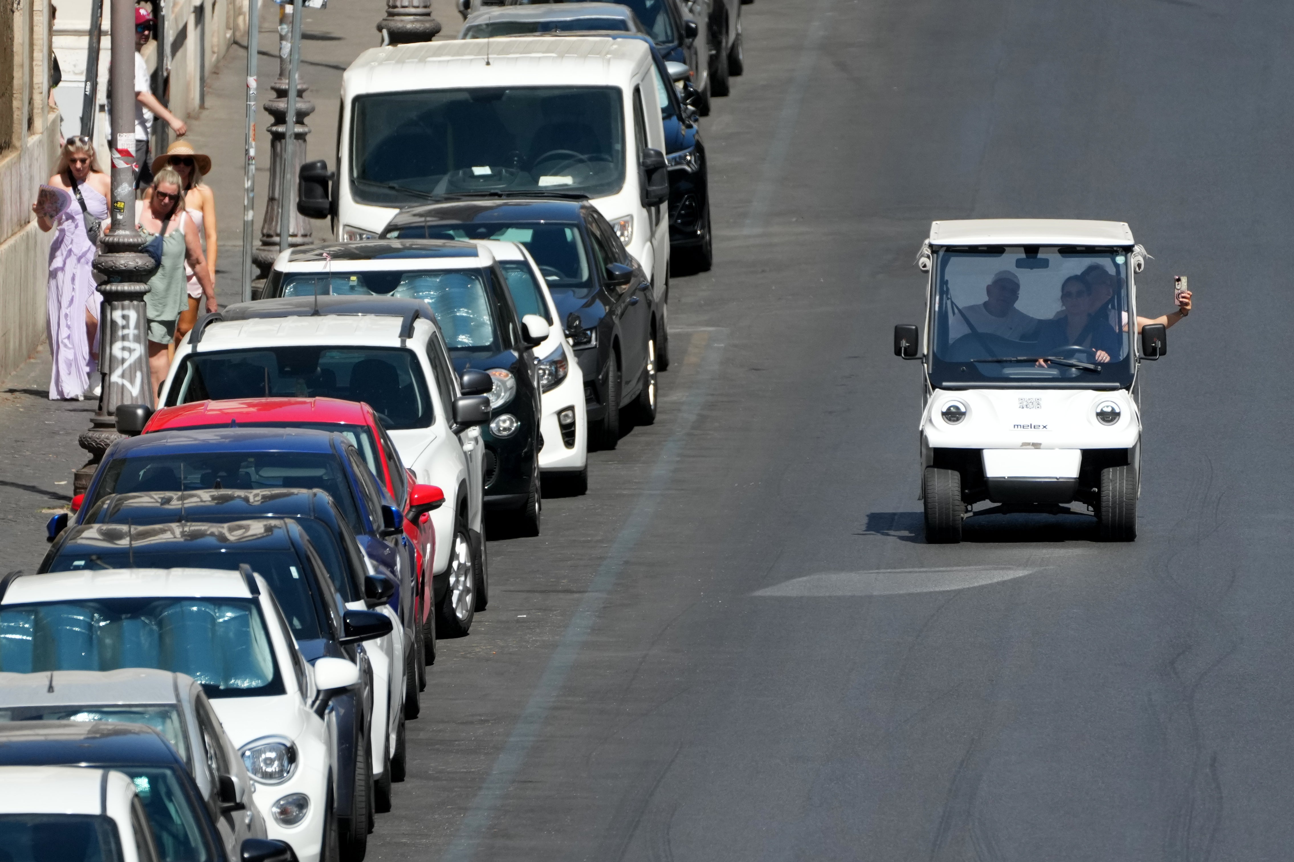 A golf cart carrying tourists travels past parked cars in Rome, Tuesday, Aug. 18, 2026 (AP Photo/Gregorio Borgia)