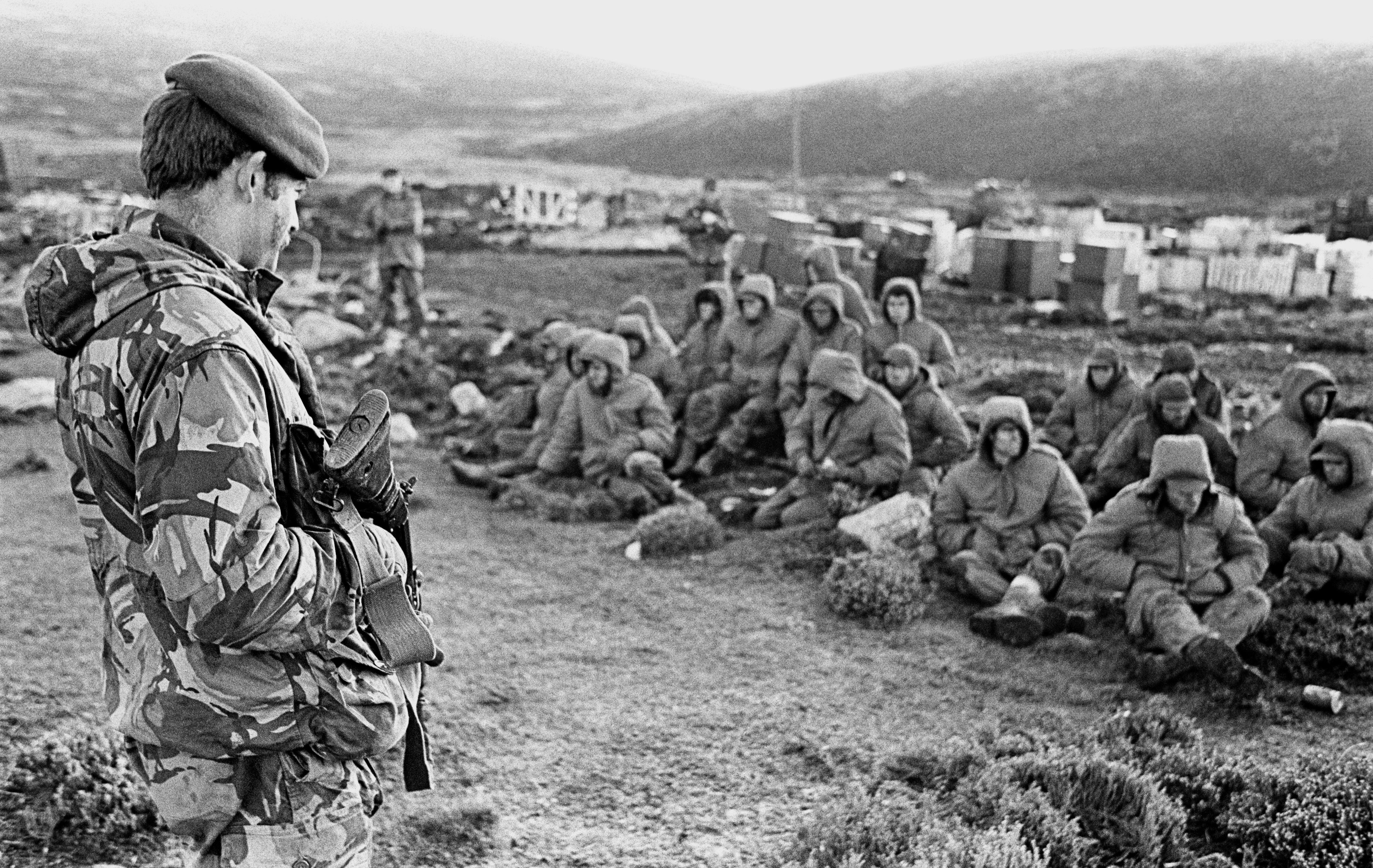 Argentinian soldiers captured at Goose Green guarded by a Royal Marine - June 2, 1982