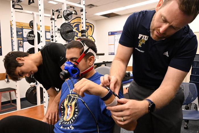 Florida International University Professor Jason Kostrna, right, reviews calorie data on four smartwatches worn by Ph.D. student Daimien Campos as he rides a stationary bike. Kostrna says a study shows smartwatches overcount calories burned during exercise