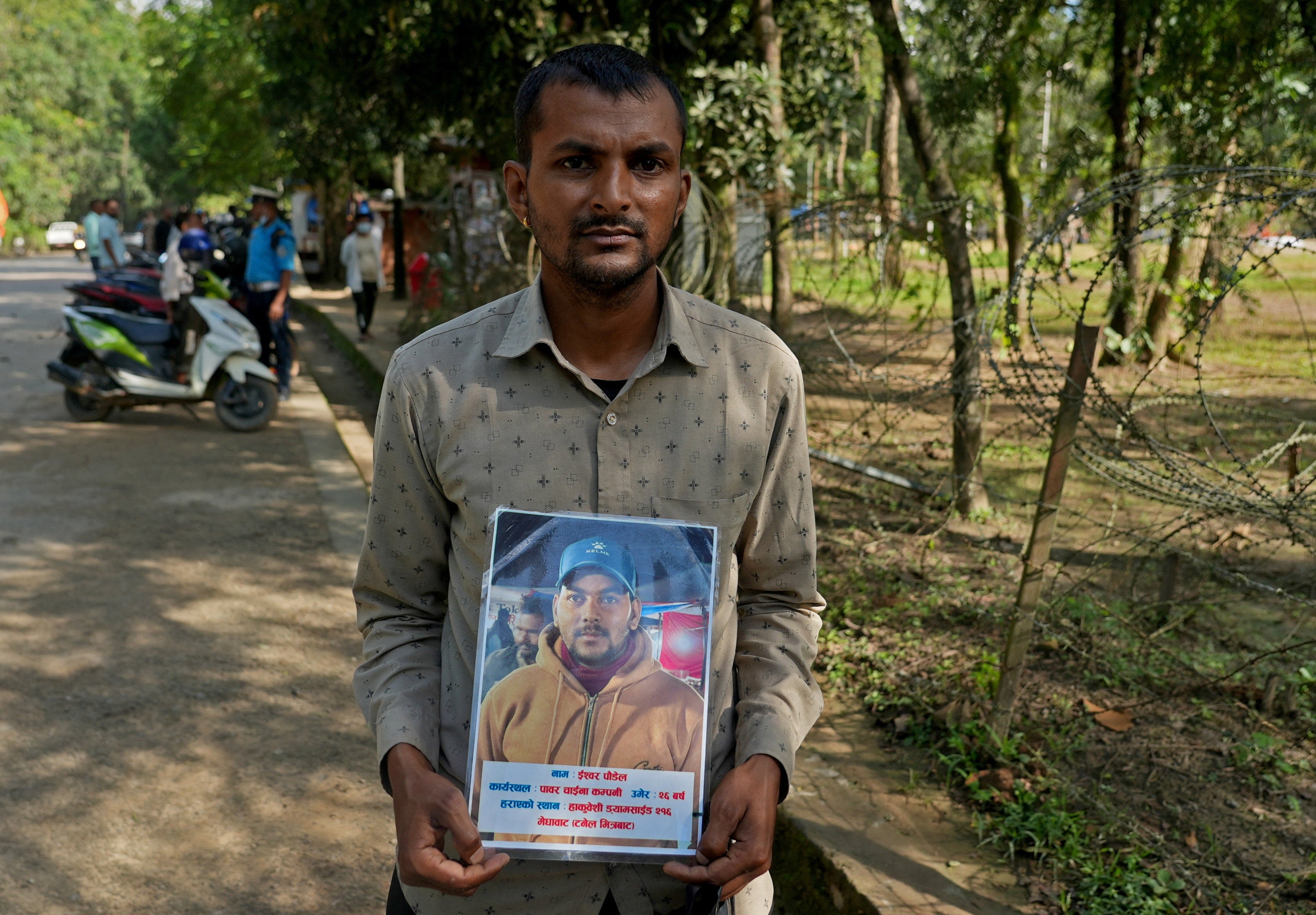 Krishna Poudel, 34, the brother of Ishwor Poudel, a missing worker at Trishuli-1 Hydropower Project, with a photograph of Ishwor outside the Maithili Barrack in Nuwakot District, Nepal