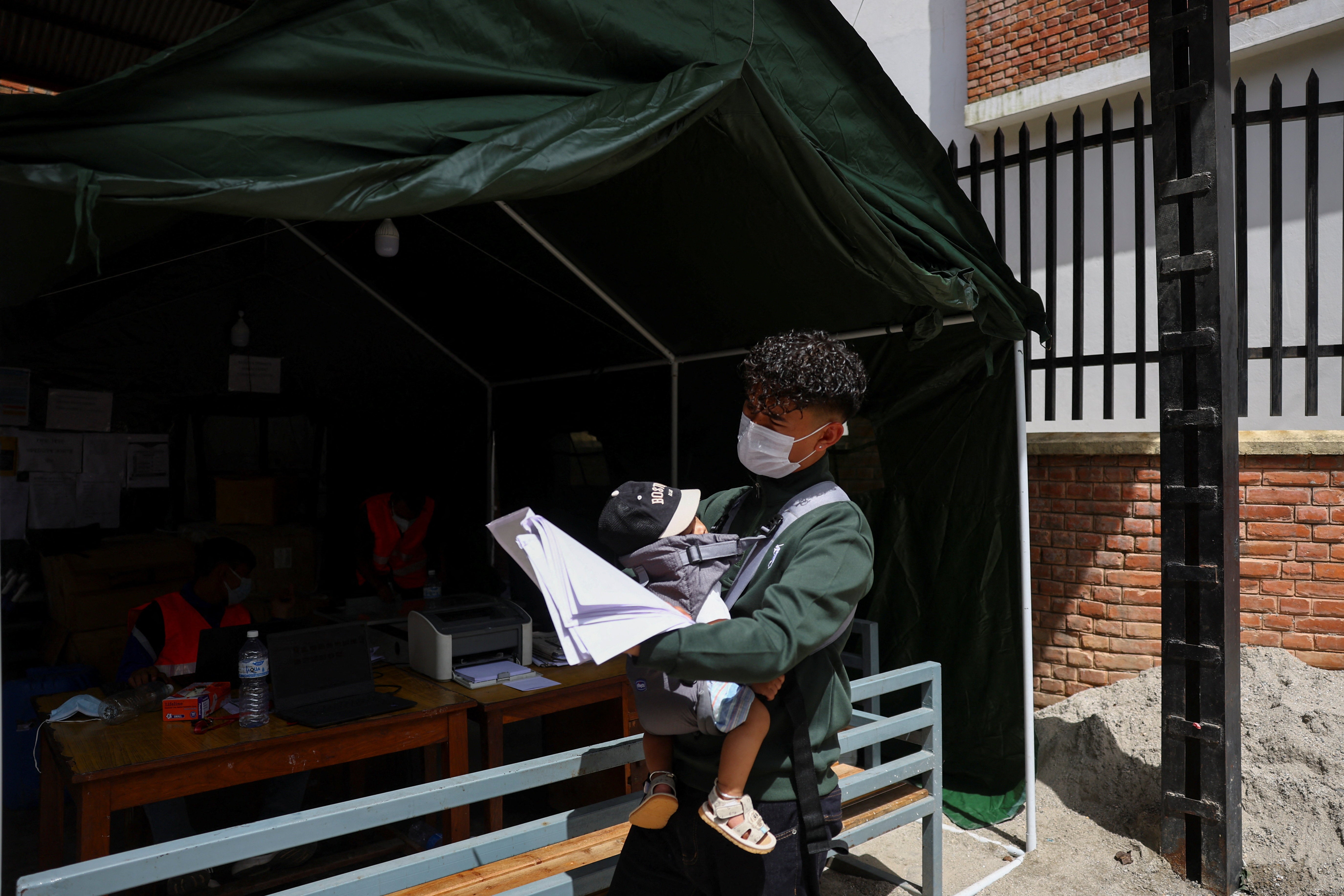 A man carries a baby as he checks through printouts of dead bodies at the post-mortem section of Maharajgunj Medical Campus (Reuters)