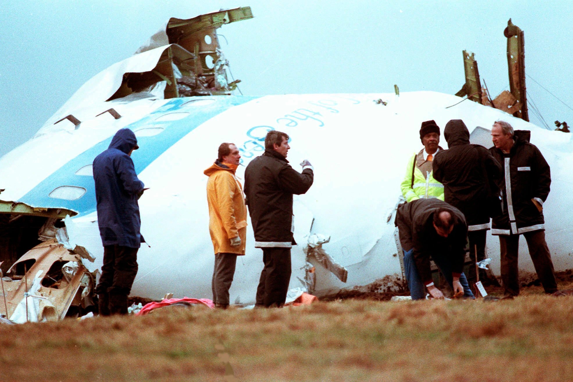 Unidentified crash investigators inspect the nose section of the crashed Pan Am flight 103, a Boeing 747 airliner in a field near Lockerbie, Scotland, Dec. 23, 1988