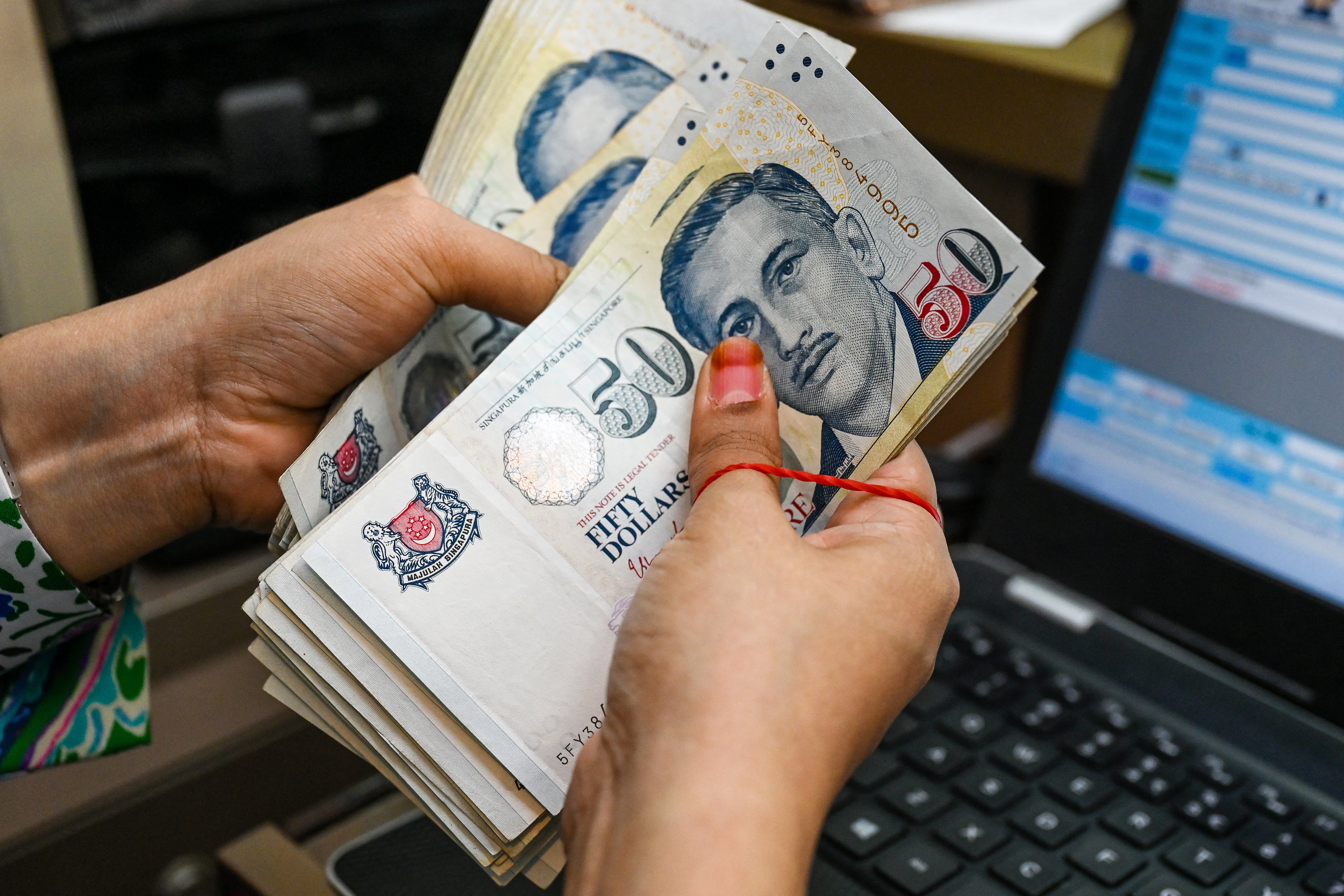 A staff counts Singapore dollar currency notes at a money changer booth at Raffles Place financial business district in Singapore