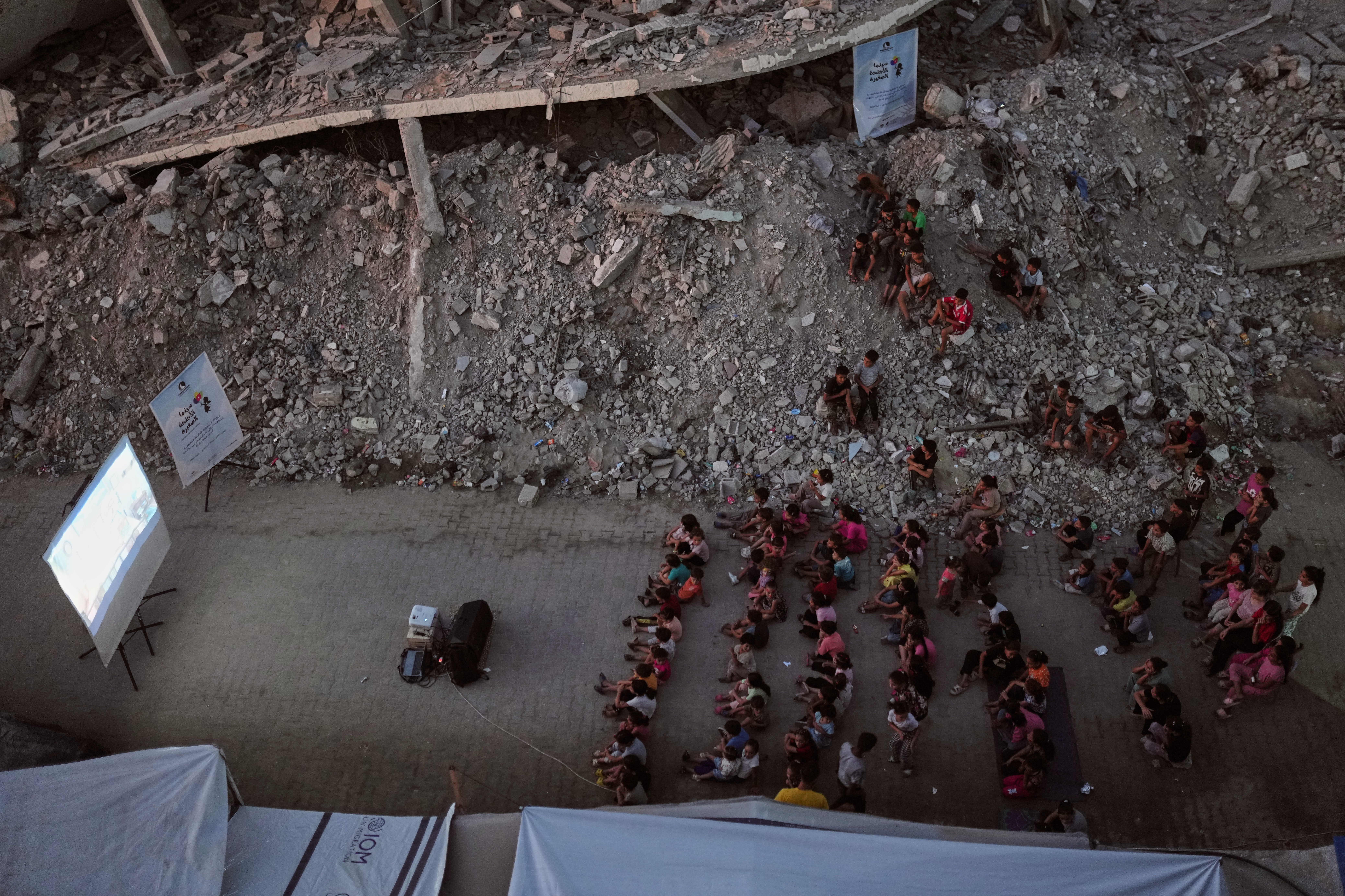 Displaced Palestinian children watch a movie amid the ruins of buildings destroyed by Israeli airstrikes