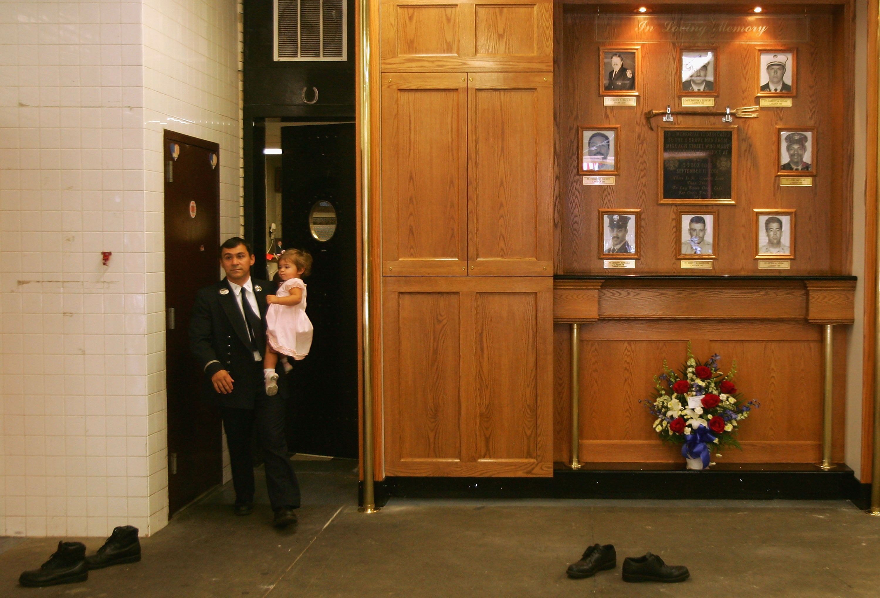 A firefighter carries his daughter past the wall of remembrance for firefighters from Ladder 118 and Engine 205 inside the Middagh Street firehouse in New York City’s Brooklyn Heights neighborhood on September 11, 2006